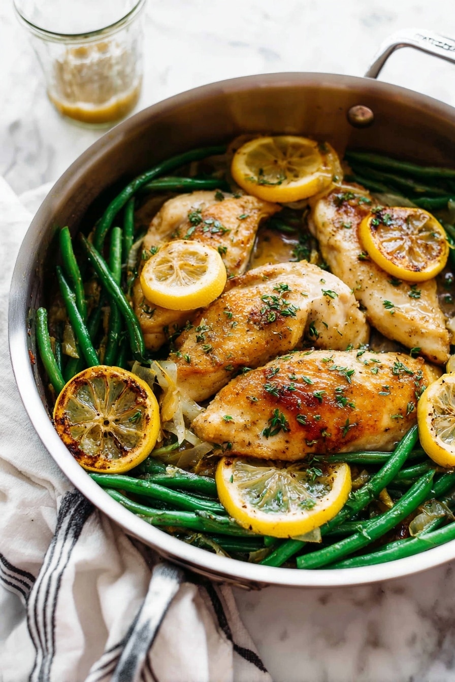 A round silver pan holds a dish with three light golden brown cooked chicken pieces on top. Underneath and around the chicken are bright green beans and several round slices of cooked lemon that are golden and slightly charred on the edges. The chicken is sprinkled with small green herb pieces and has a slightly shiny sauce coating parts of it. The pan is placed on a white marbled surface, with a white cloth with black stripes in the back left and a glass cup with some sauce behind the pan. Photo taken with an iphone --ar 2:3 --v 7 - Garlic Lemon Butter Chicken Skillet, Lemon Butter Chicken, Crispy Parmesan Chicken, Easy Chicken Skillet Dinner, Weeknight Chicken Recipes