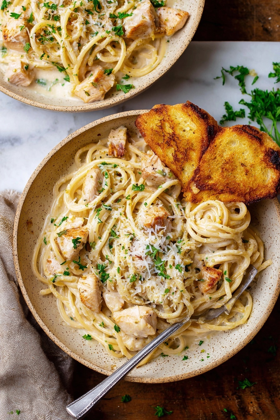 A close-up view of creamy pasta shows thick spaghetti strands coated in a smooth, light beige sauce. Mixed in are small chunks of grilled light brown chicken, with specks of black pepper and green parsley leaves scattered on top. A white piece of bread with a golden-brown crust rests on the side of the plate. A black fork is twirling some noodles and chicken. The plate has a rustic look with a speckled edge and sits on a white marbled surface. photo taken with an iphone --ar 2:3 --v 7 - Garlic Parmesan Chicken Pasta, creamy chicken pasta, easy chicken pasta recipe, quick dinner pasta, restaurant-style pasta