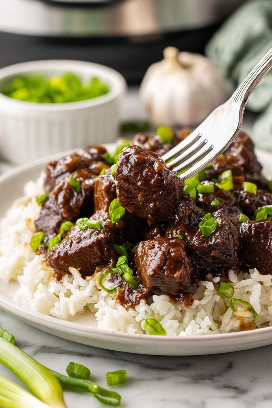 The dish shows a single white plate on a white marbled table, holding two main layers: the bottom layer is white rice with some chopped green onions scattered on top, and the top layer is dark brown beef chunks covered in a shiny glaze, also garnished with green onions. A silver fork pierces one beef chunk in the center of the plate, lifting it slightly above the rest. In the background, a whole garlic bulb and a small white bowl with more green onions are partially visible, adding to the kitchen setting. Photo taken with an iphone --ar 2:3 --v 7 - Honey Garlic Steak Bites, savory steak bites, easy steak recipes, quick dinner ideas, flavorful beef dishes