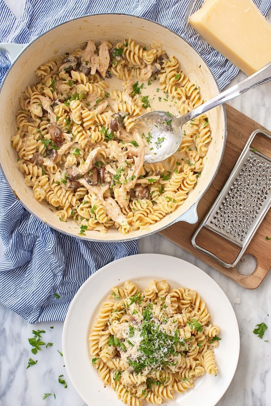 A white pot filled with creamy cooked rotini pasta mixed with light brown cooked chicken strips and small brown mushrooms, sprinkled with fresh green chopped herbs on top, a silver spoon rests inside the pot lifting some pasta. Below the pot, there is a white plate with a serving of the same pasta topped with more green herbs and a light sprinkle of grated cheese. To the side, a block of light yellow cheese and a metal grater rest on a blue striped cloth, all placed on a white marbled surface. photo taken with an iphone --ar 2:3 --v 7 - Creamy Leftover Turkey Pasta, leftover turkey pasta recipes, quick turkey pasta dinner, easy holiday turkey ideas, comforting turkey pasta