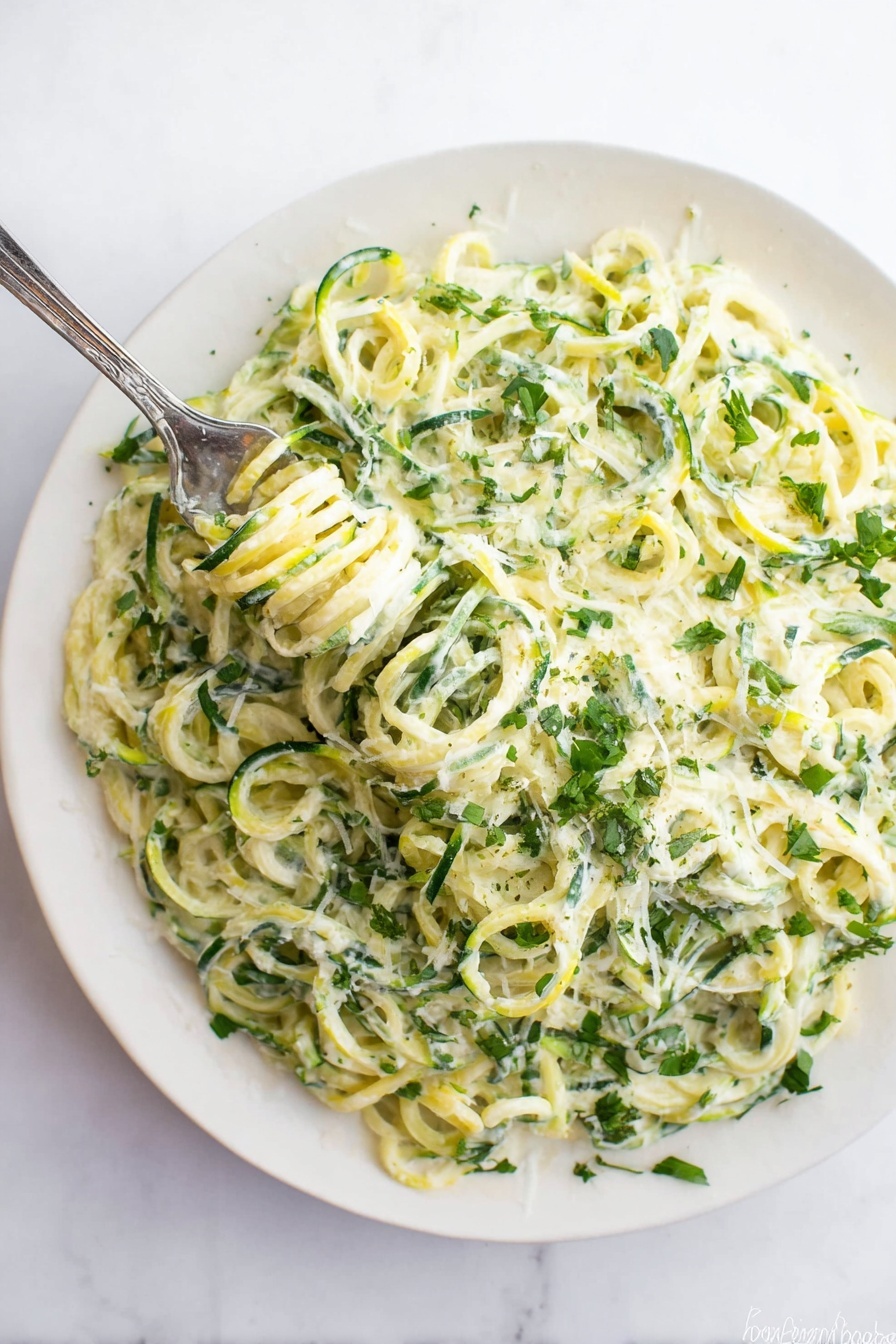A white plate filled with a creamy dish made of spiral-shaped green and light yellow vegetable noodles, mixed with a white creamy sauce that coats the noodles evenly. There are small green herb leaves sprinkled throughout the dish, adding a fresh look. A silver fork is twirling some of the noodles in the top left area of the plate. The plate rests on a white marbled surface. photo taken with an iphone --ar 2:3 --v 7 - Zucchini Alfredo Cream Pasta, healthy zucchini pasta, easy Alfredo sauce recipe, quick dinner ideas, low-carb pasta alternatives