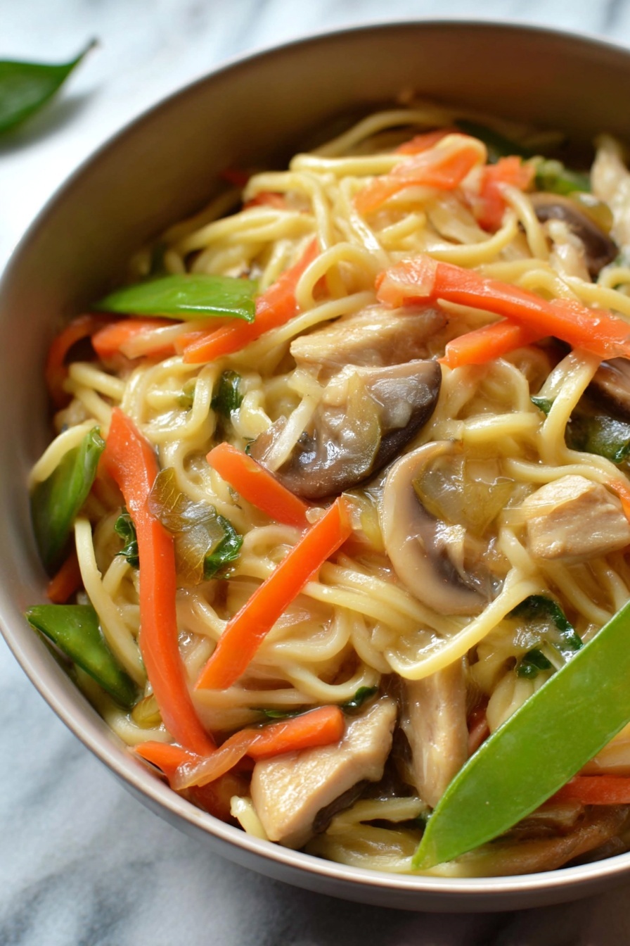 A close-up shot of a round white bowl filled with a noodle dish that has three main visible layers. The base layer consists of light yellow noodles that look soft and slightly shiny. Mixed in and on top of the noodles are bright orange thin carrot strips, pale green sliced snow peas, and light brown sliced mushrooms. Scattered throughout are small pieces of light brown cooked chicken or tofu, adding texture contrast. The background shows an out-of-focus white marbled surface, giving the dish a clean and fresh look. Photo taken with an iphone --ar 2:3 --v 7 - Instant Pot Chicken Lo Mein, quick Chinese stir-fry, easy chicken noodle dinner, weeknight Instant Pot recipes, savory noodle dishes
