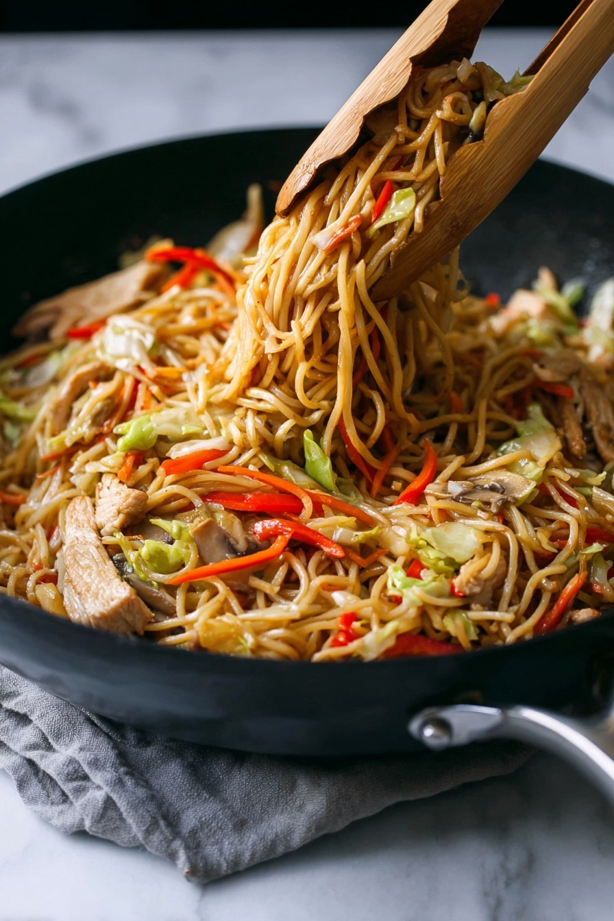 A close-up of a black skillet filled with cooked stir-fried noodles lifted by wooden tongs, showing three main layers: a base layer of thin, light brown noodles tangled together; mixed throughout are slices of light beige cooked meat and strips of vegetables including red bell peppers, pale green cabbage, thin orange carrot sticks, and light brown mushrooms. The noodles have a slightly shiny texture, and the colors of the vegetables add bright, fresh contrast. The skillet rests on a white marbled surface with a subtle grey cloth partially visible under the handle. photo taken with an iphone --ar 2:3 --v 7 - Chicken Yakisoba Stir-Fry, Chicken Yakisoba, stir-fry dinner, Japanese-style noodle recipe, easy Japanese stir-fry