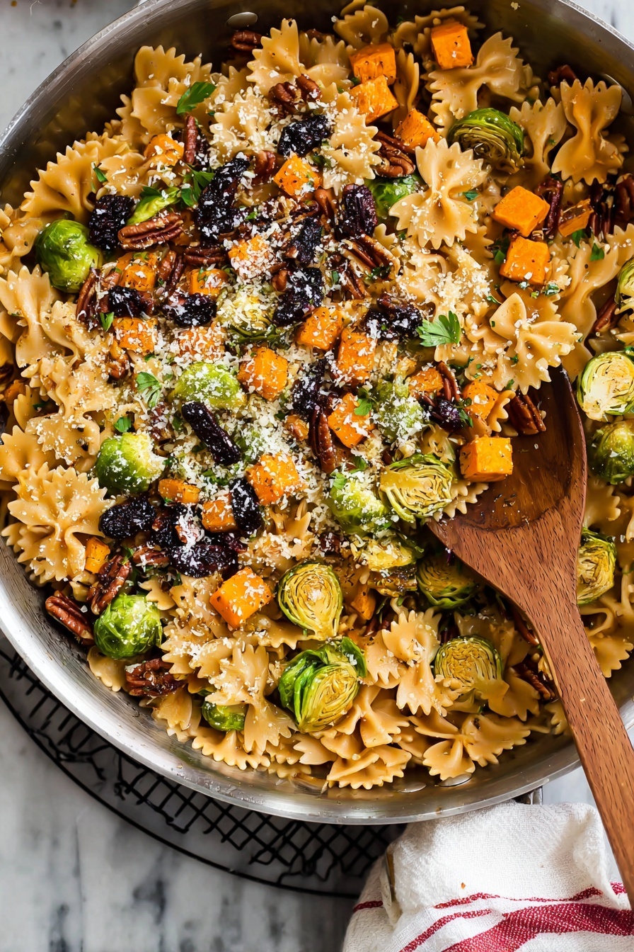 A large silver pan filled with a colorful pasta dish featuring three layers: the bottom layer has light brown farfalle pasta with smooth, slightly shiny texture; the middle layer contains bright orange small cubed roasted vegetables and sliced green brussels sprouts, some with charred marks, scattered evenly; the top layer is sprinkled with chopped dark brown pecans, black dried fruit pieces, small green herb leaves, and a light dusting of finely grated white cheese. A wooden spoon with a rounded bowl sits inside the pan. The pan rests on a black wire rack with a white cloth with red stripes on the side, all set on a white marbled surface. Photo taken with an iphone --ar 2:3 --v 7 - Brussels Sprouts Pasta with Brown Butter, Brussels Sprouts Pasta, brown butter pasta recipes, fall vegetable pasta, easy weeknight pasta