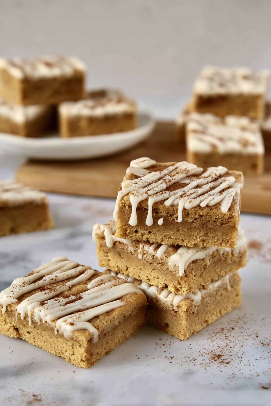 A stack of four square bars sits on a white marbled surface, each bar having a light golden brown color with a soft, crumbly texture. The bars are topped with lines of white icing dripping down the sides, and a sprinkling of fine brown powder. Nearby, a single bar lies flat, showing its thick layer and the decorated top. In the background, more bars with the same look rest on a white plate and a wooden board, all against a blurred white marbled texture background. photo taken with an iphone --ar 2:3 --v 7 - Cinnamon Sugar Blondies, cinnamon blondies, easy blondie recipe, cinnamon dessert, sweet blondie bars