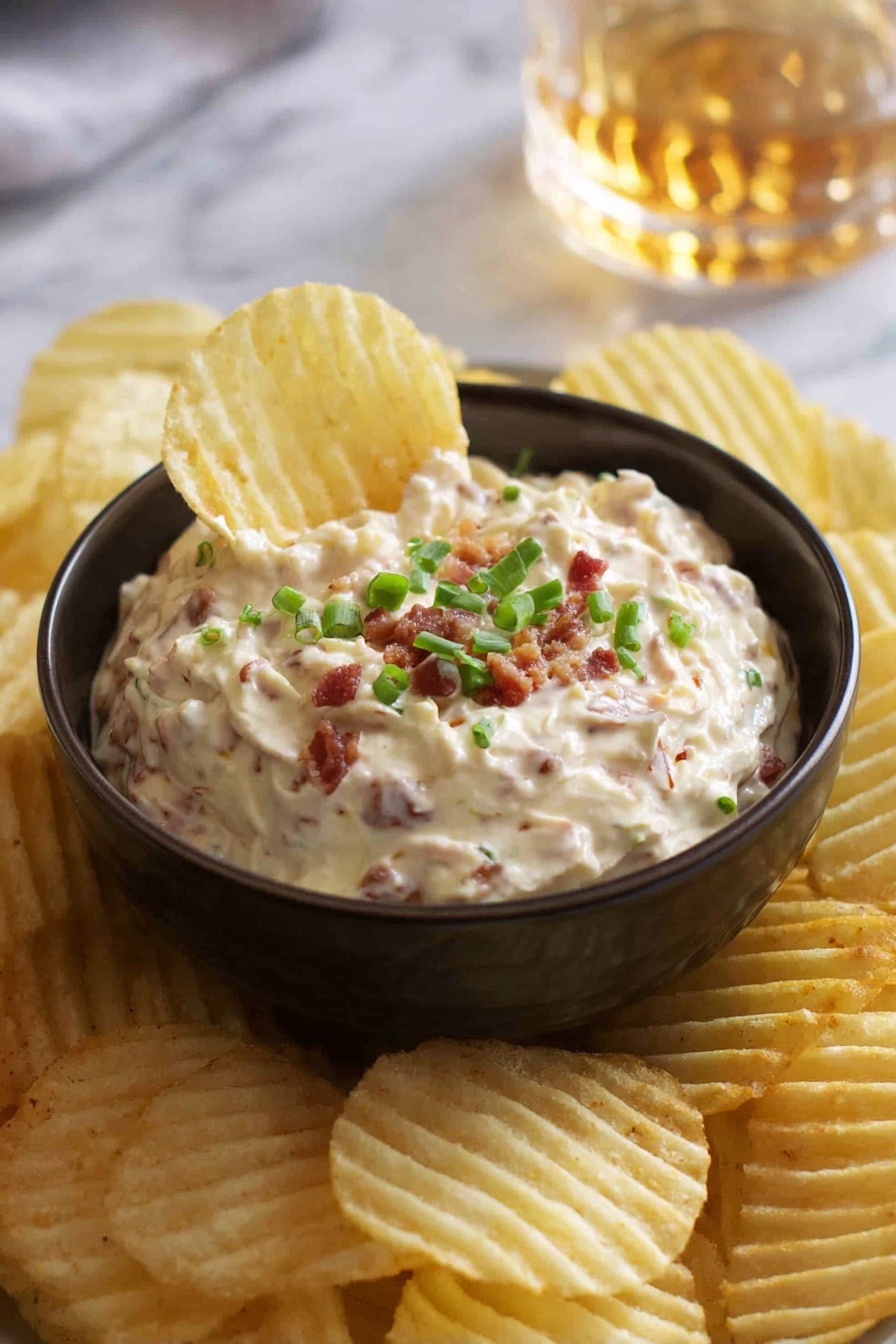 A small dark bowl filled with creamy dip that has small pieces of bacon mixed in, topped with chopped green onions. The bowl sits on a white marbled surface and is surrounded by many ridged potato chips, one chip is dipped into the bowl showing the texture of the dip. In the background, there is a blurred glass with a golden liquid. Photo taken with an iphone --ar 2:3 --v 7 - Homemade French Onion Dip, French Onion Dip, caramelized onion dip, creamy onion dip, party dip recipes