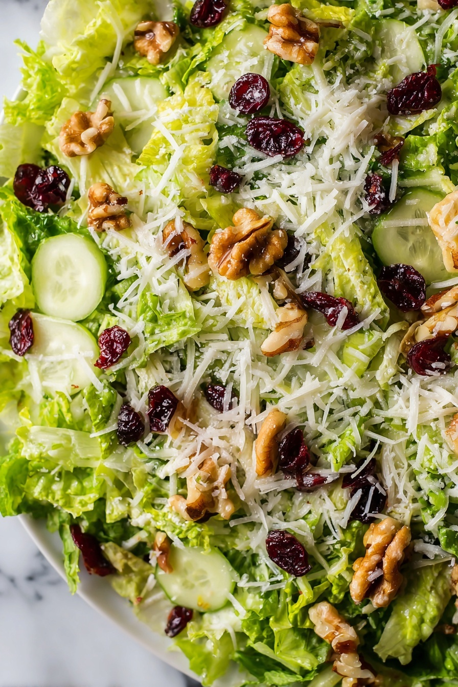 The image shows a close-up view of a fresh salad with several layers. The base layer consists of thinly shredded bright green lettuce. Scattered on top are thin slices of pale green cucumber, adding a smooth texture. There are pieces of light brown walnuts sprinkled across, giving a rough, chunky look. Interspersed are small dark red dried cranberries providing contrasting color and texture. The final layer is a light dusting of white shredded cheese spread evenly over the top. The salad is on a white plate placed over a white marbled surface. photo taken with an iphone --ar 2:3 --v 7 - Brussels Sprouts Apple Cranberry Salad, seasonal healthy salad, holiday veggie salad, apple cranberry Brussels sprouts, festive winter salad