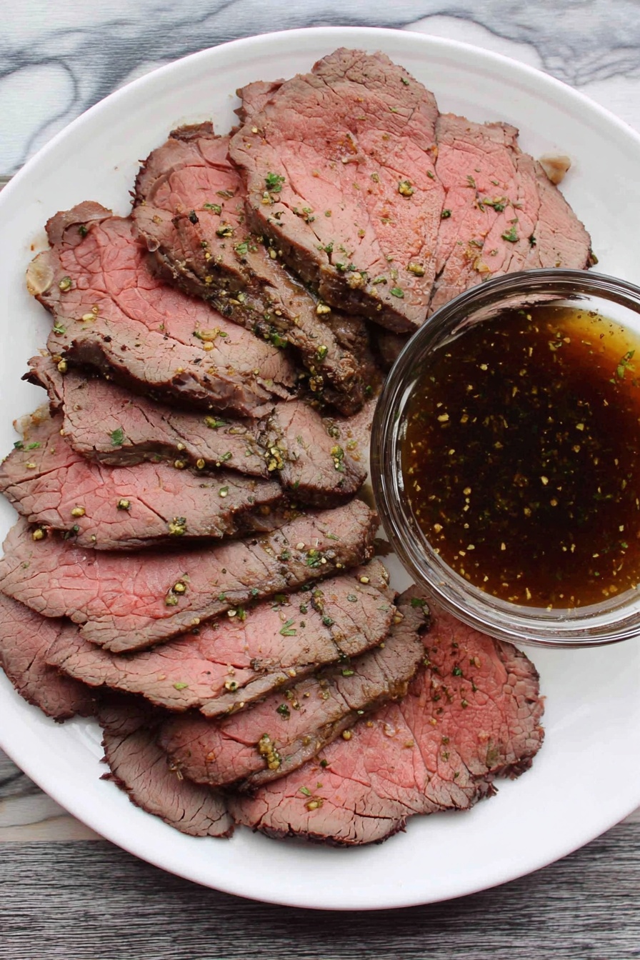 A white plate filled with several thin slices of roast beef, showing pink centers and darker brown edges with visible seasoning and small green herb bits. On the side of the plate, there is a clear glass bowl filled with a dark brown, speckled dipping sauce. The plate is placed on a white marbled surface. photo taken with an iphone --ar 2:3 --v 7 - Perfect Roast Beef Top Round, roast beef recipe, tender roast beef, easy beef roast, juicy beef dinner
