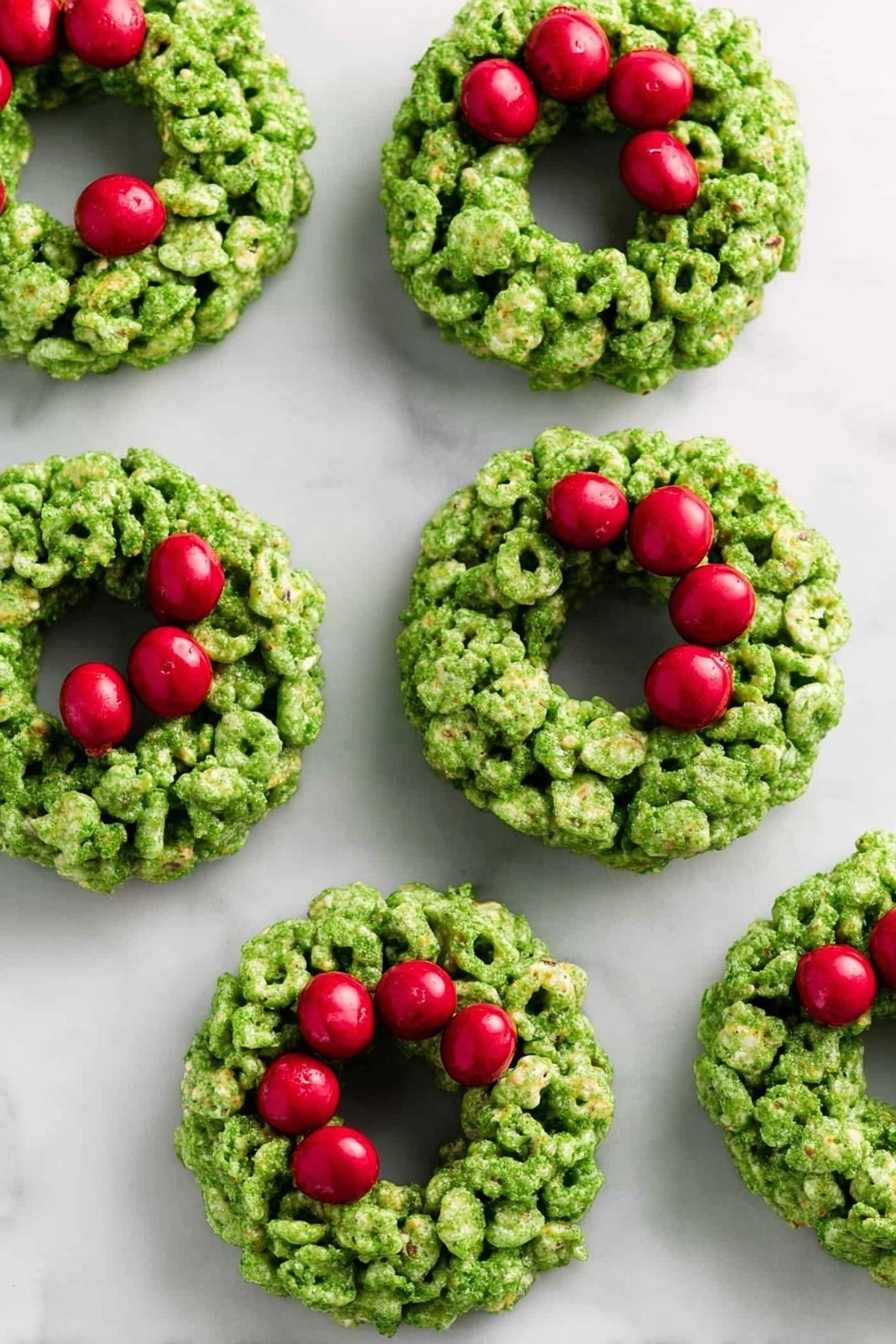 The image shows seven small green wreath-shaped treats placed on a white marbled surface. Each wreath is made from clusters of green cereal pieces stuck together, forming a thick ring with a hollow middle. Bright red round candies are grouped in threes on the top right side of each wreath, resembling berries on a holiday decoration. The green cereal has a rough texture with some visible cornflakes, and the red candies look smooth and shiny. The overall look is festive and colorful, with the wreaths evenly spaced across the surface. photo taken with an iphone --ar 2:3 --v 7 - Cornflake Wreaths, holiday treat ideas, festive Christmas treats, quick holiday snacks, easy no-bake holiday desserts