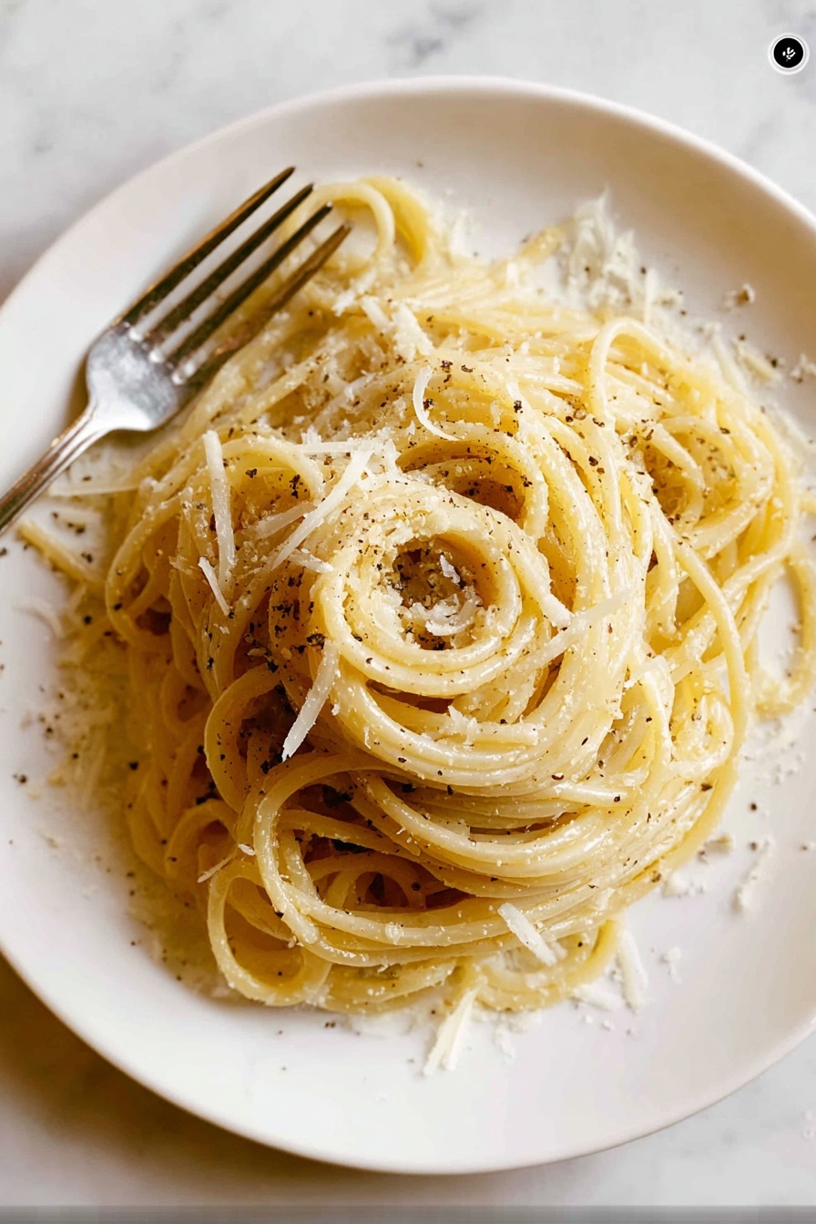 A white round plate holds a neatly twirled mound of spaghetti pasta as the main layer, pale yellow in color with a slight shine. Scattered over the pasta are small, irregular shreds of white cheese that add texture and light contrast to the smooth noodles. Black pepper flakes are sprinkled lightly, creating small dark spots across the dish. To the left side of the plate, a silver fork is partially visible, resting beside the pasta. The background has a white marbled texture, creating a clean and simple setting. Photo taken with an iphone --ar 2:3 --v 7 - Easy Cacio e Pepe Pasta, classic Roman pasta, quick Italian pasta recipe, cheesy pepper pasta, simple pasta dishes