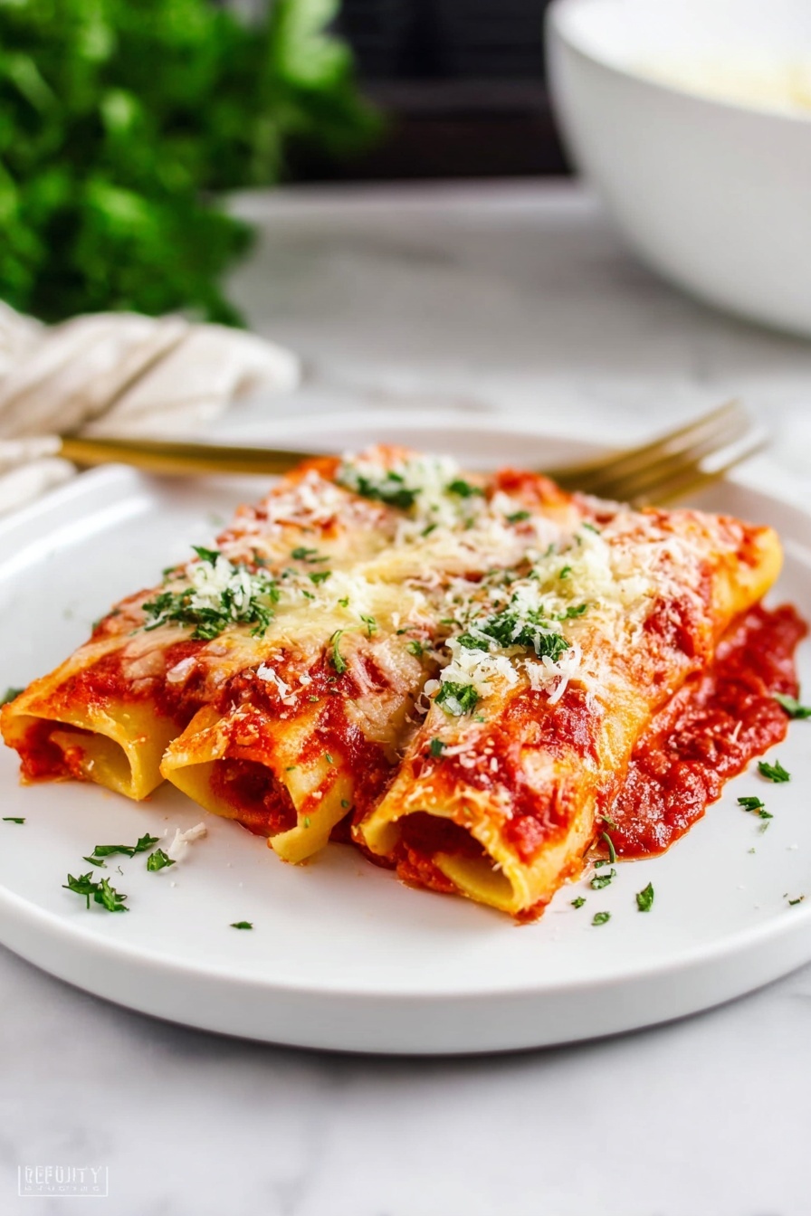 The image shows three rolled pasta pieces placed side by side on a large white plate, each covered in a thick red tomato sauce and melted white cheese that is slightly browned. There is a sprinkle of finely grated white cheese and fresh green herbs evenly scattered over the pasta. In the background, there is a white bowl with green herbs and a tray with more pasta rolls visible on a dark surface, all set on a white marbled texture. To the right of the plate, there is a golden spoon and fork resting on the same dark surface. Photo taken with an iphone --ar 2:3 --v 7 - Cheese Manicotti, cheese manicotti recipe, Italian cheese manicotti, baked cheese manicotti, cheesy manicotti pasta