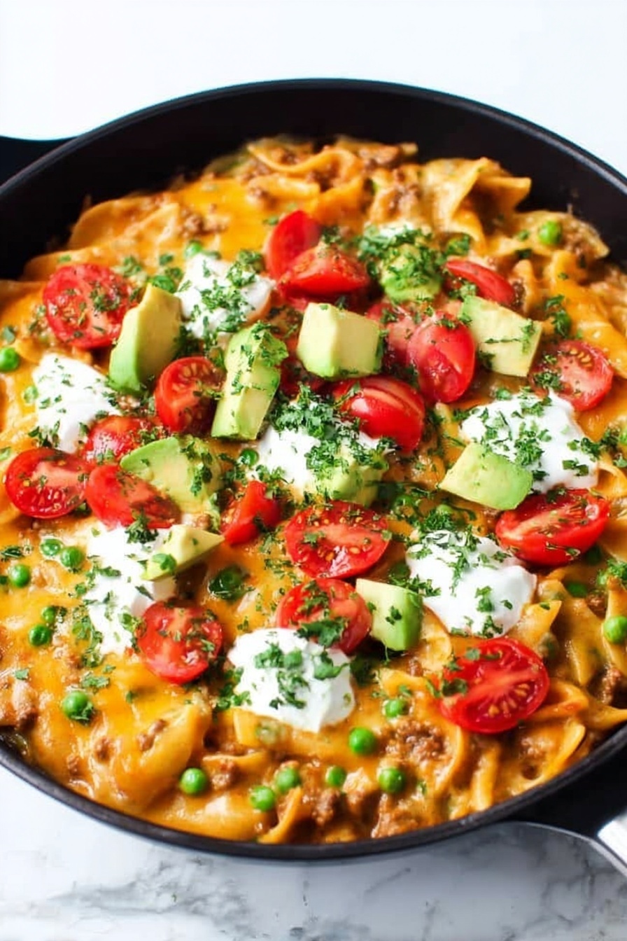 A black cast iron pan filled with a layered baked pasta dish topped with melted bright orange cheese, scattered green chopped herbs, and chopped green onions. On top are halved red cherry tomatoes, chunks of light green avocado, and dollops of white sour cream. A wooden spoon is scooping some of the pasta from the right side, showing short tube-shaped pasta mixed with meat and sauce underneath the cheese layer. The whole scene is set on a white marbled surface. photo taken with an iphone --ar 2:3 --v 7 - Cheesy Enchilada Pasta Skillet, cheesy enchilada pasta, easy enchilada pasta dinner, quick pasta skillet, one-pot enchilada pasta