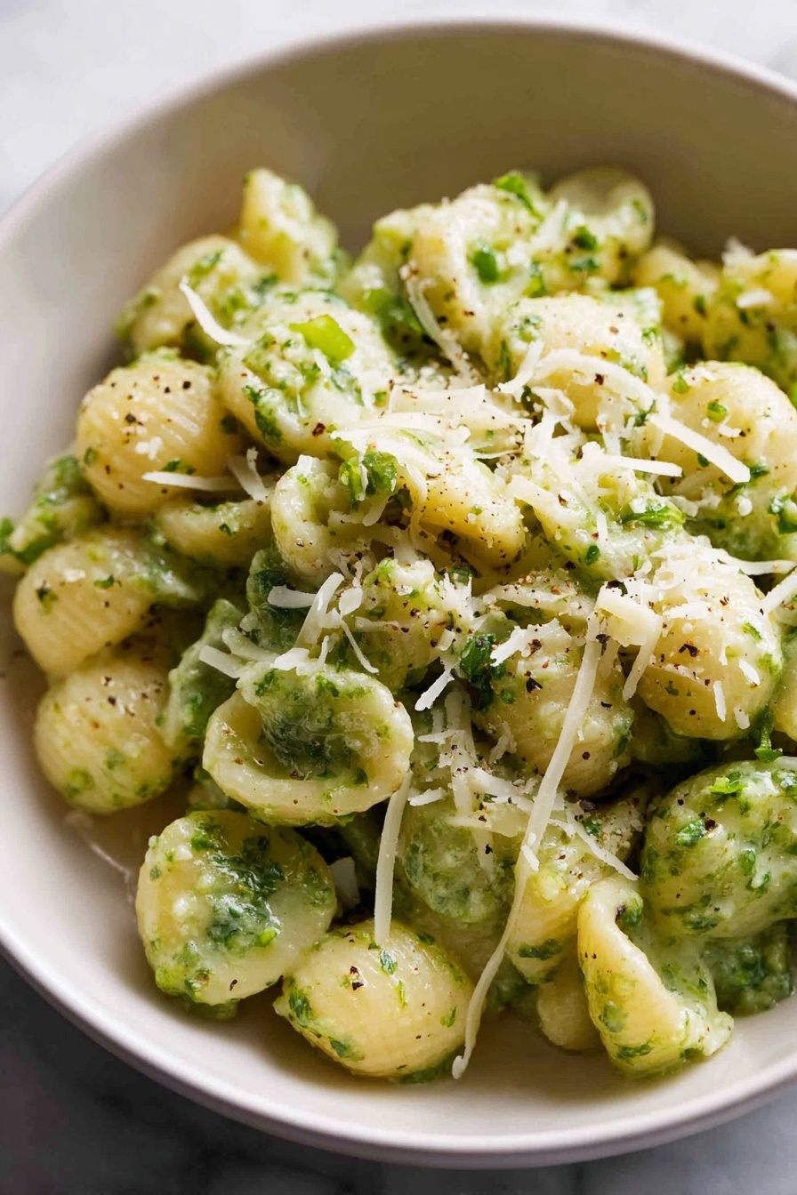 A large bowl filled with small spiral pasta mixed with bright green broccoli florets. The pasta is light yellow and looks soft, while the broccoli pieces are spread evenly throughout the dish. On top, there is a sprinkling of grated parmesan cheese, adding a slight white textured layer. A silver spoon is placed inside the bowl on the left side, ready to serve. In the background, there are two stacked white bowls, a silver fork and spoon set on a white cloth, and a block of parmesan cheese next to a grater on a white marbled surface. The overall setting feels cozy and inviting. photo taken with an iphone --ar 2:3 --v 7 - Quick Broccoli Pasta with Lemon and Cheese, healthy quick pasta recipes, easy broccoli pasta dinner, speedy veggie pasta, lemon cheese pasta dish