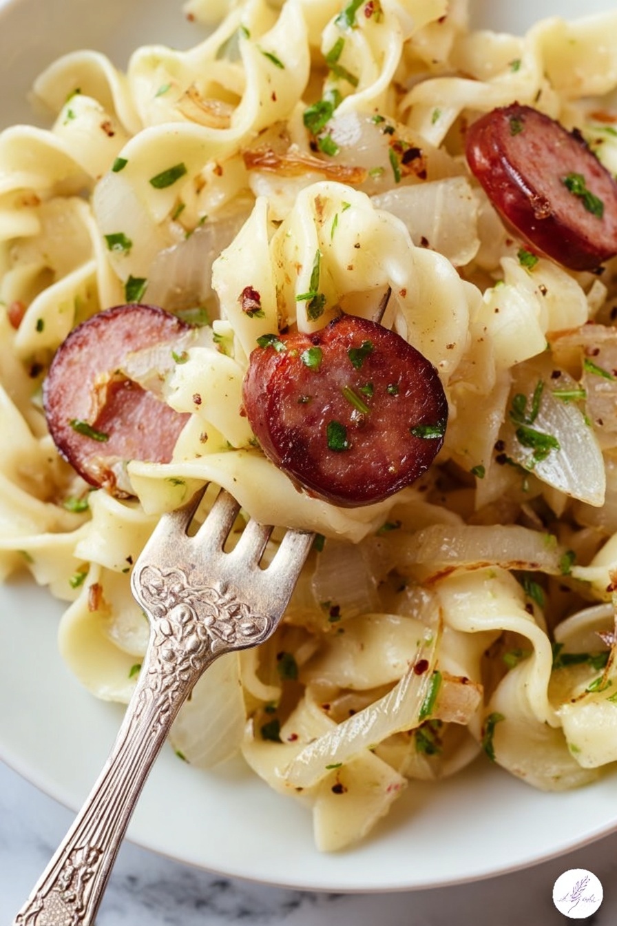 A close-up view of a white plate filled with twisted egg noodles that are light yellow with a soft texture, mixed with small pieces of cooked onions that are translucent white with a slight brown edge, and slices of browned sausage that are dark red with a grilled surface and visible herbs. The noodles and ingredients are sprinkled with chopped green herbs and black pepper. A vintage silver fork with floral engravings is lifting some noodles and one slice of sausage. The background is a white marbled surface. Photo taken with an iphone --ar 2:3 --v 7 - Kielbasa and Cabbage Haluski, kielbasa cabbage skillet, hearty comfort food recipes, easy sausage and cabbage dish, quick weeknight dinners