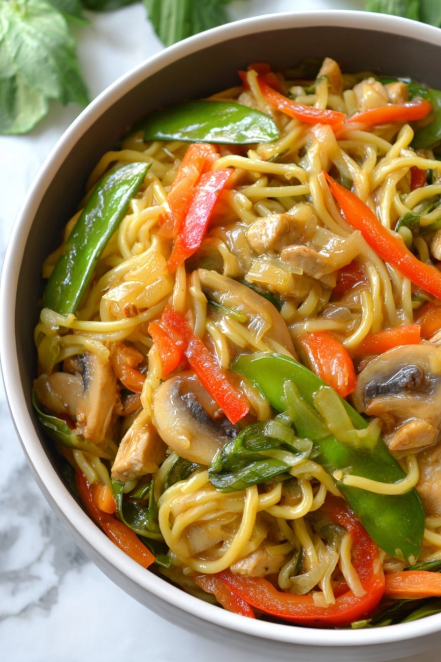 The image shows a close-up of a bowl filled with a colorful noodle stir-fry. The bottom layer consists of long, light yellow noodles, mixed evenly with sliced vegetables including bright green snow peas, orange thin carrot strips, chunky red bell pepper pieces, and light brown mushroom slices. There are also pieces of light tan tofu or chicken mixed into the dish. The noodles and vegetables are coated with a glossy sauce, giving them a shiny and slightly wet texture. The bowl is white, and it sits on a white marbled surface with some green leaves blurred in the background. photo taken with an iphone --ar 2:3 --v 7 - Instant Pot Chicken Lo Mein, quick Chinese stir-fry, easy chicken noodle dinner, weeknight Instant Pot recipes, savory noodle dishes