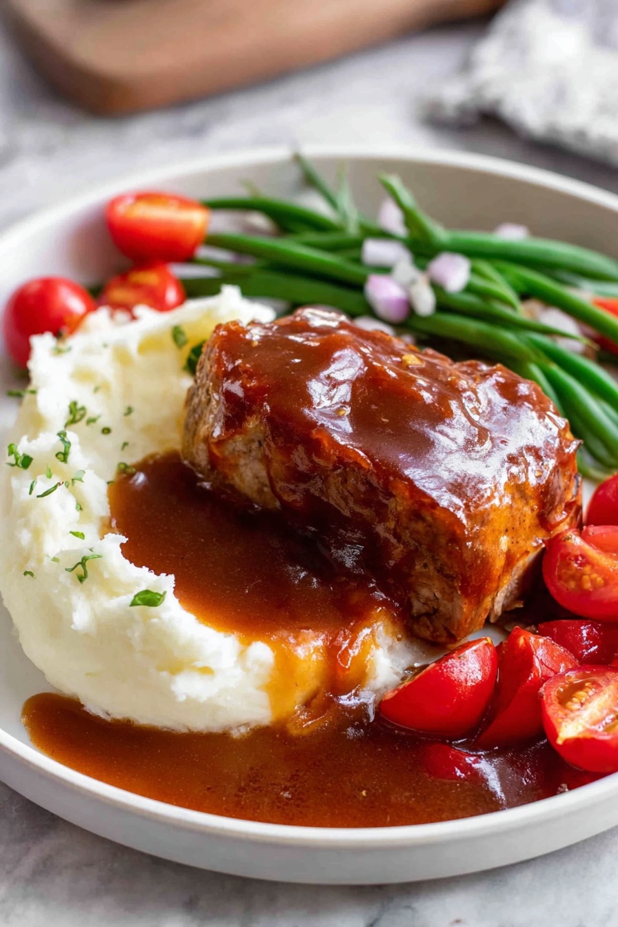 A white plate shows a thick layer of smooth white mashed potatoes on the left side, topped with a glossy brown sauce that pools around the dish. On top of the potatoes sits a piece of cooked meat covered in the same brown sauce, with a slice cut to reveal the inside texture. Behind the meat, there is a row of green beans and bright red cherry tomato halves scattered around, garnished with small pieces of chopped onions. The plate rests on a white marbled surface. Photo taken with an iphone --ar 2:3 --v 7 - Oven BBQ Chicken with Homemade Sauce, BBQ chicken baked in oven, easy oven baked BBQ chicken, tender oven BBQ chicken recipe, homemade BBQ sauce chicken