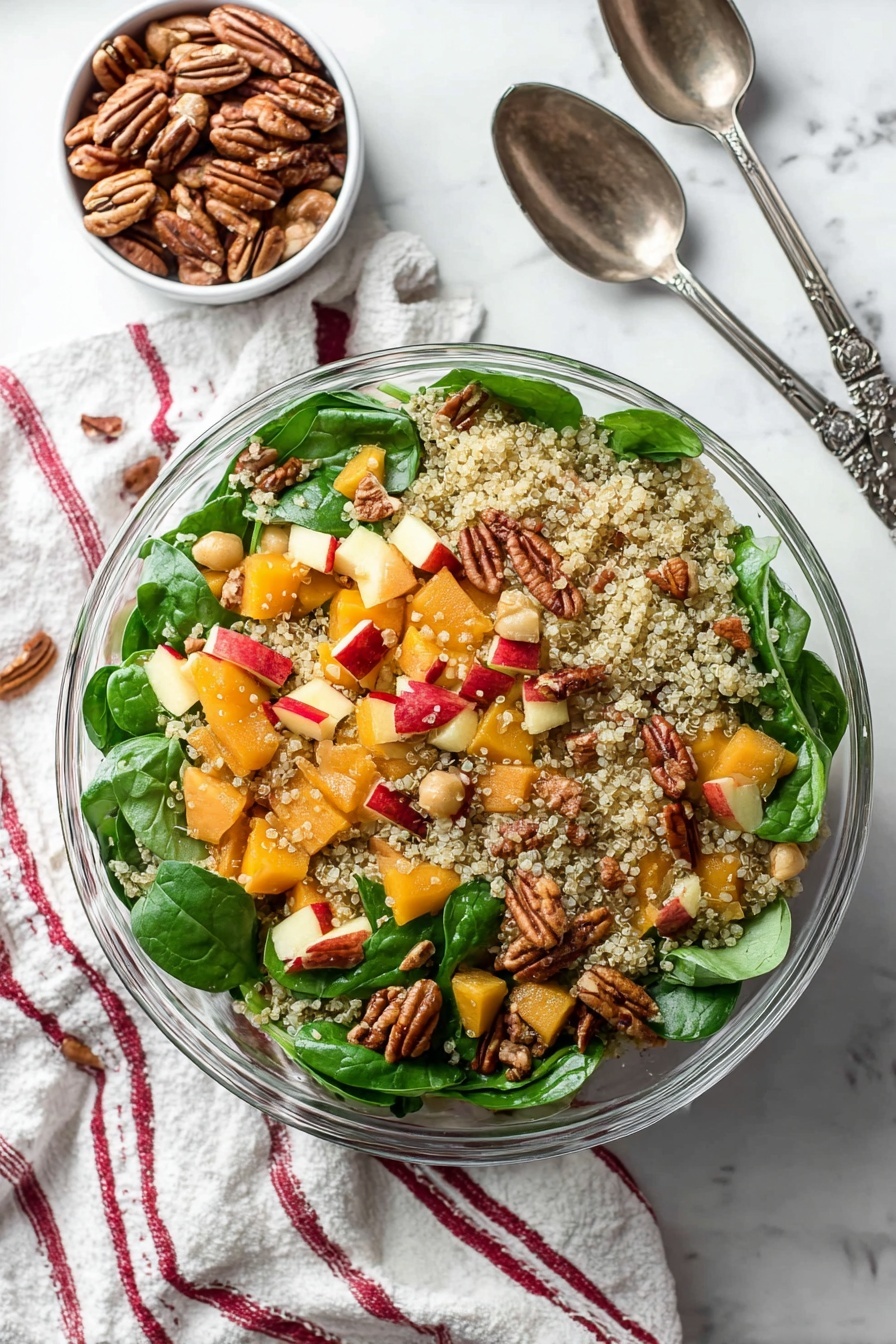 This image shows a clear glass bowl filled with a colorful quinoa salad. The base layer is light, fluffy quinoa with small, round grains scattered evenly throughout. Mixed inside are bright green fresh spinach leaves with a smooth texture, orange chunks of butternut squash, and small pale beans adding softness. Red-skinned apple pieces give a splash of red color, and whole pecans add a textured, brown, nutty layer randomly placed on top. The bowl is on a white marbled surface with a soft striped cloth nearby, and a woman's hand holds a dark metal salad spoon at the edge. photo taken with an iphone --ar 2:3 --v 7 - Roasted Butternut Squash Quinoa Salad, healthy fall salads, easy quinoa salad recipes, roasted vegetable salads, nutritious winter salads