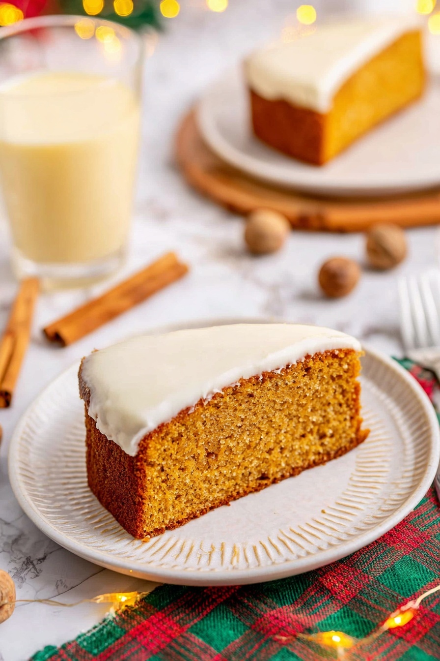 The image shows a single slice of moist, golden-brown cake with a thick layer of smooth white frosting on the bottom side, sitting on a white plate with a subtle textured rim. The cake slice has a slightly rough texture on top, indicating it is soft inside. Around the plate, there are cinnamon sticks and whole nutmegs scattered on a white marbled surface, with a colorful plaid cloth partially visible underneath. In the background, there is a clear glass filled with a light yellow creamy drink, and a second plate holding another slice of the same cake. Small warm fairy lights add a cozy touch to the scene. Photo taken with an iphone --ar 2:3 --v 7 - Eggnog Bread with Rum Glaze, Eggnog Christmas Bread, Festive Eggnog Bread, Holiday Eggnog Loaf, Rum Glazed Eggnog Dessert
