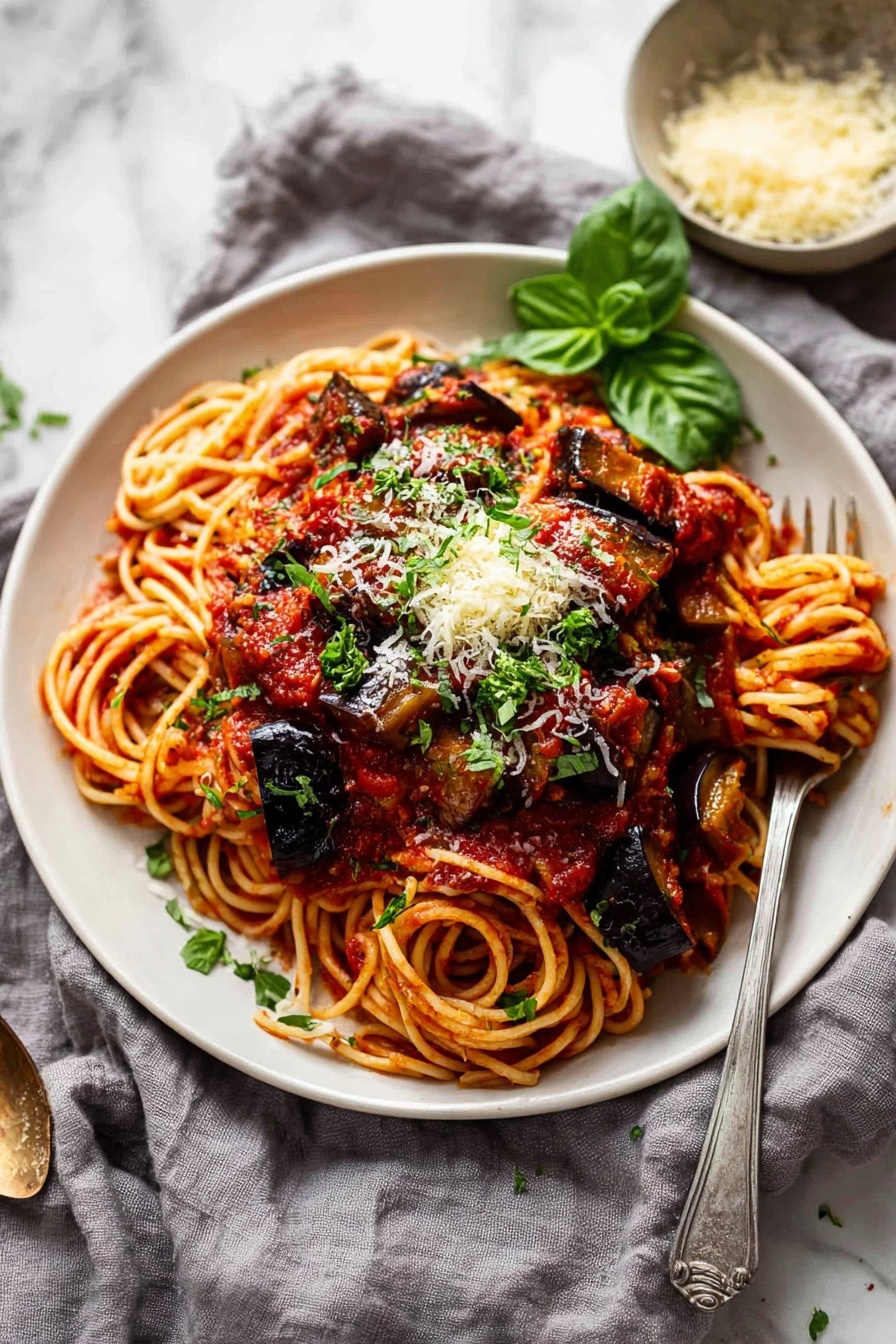 The image shows a close-up of a white bowl filled with spaghetti pasta soaked in rich red tomato sauce, with thick chunks of cooked eggplant scattered on top. The spaghetti strands are tangled at the base and coated evenly with sauce. Large pieces of dark purple eggplant, slightly charred and shiny, sit on the pasta, sprinkled with light yellow grated cheese and small green herb leaves. A silver fork is partly stuck into the pasta, lifting some strands with sauce. The bowl rests on a white marbled surface. Photo taken with an iphone --ar 2:3 --v 7 - Eggplant Pasta alla Norma, Sicilian Eggplant Pasta, authentic Eggplant Pasta, easy Eggplant Pasta recipe, flavorful Italian pasta dishes