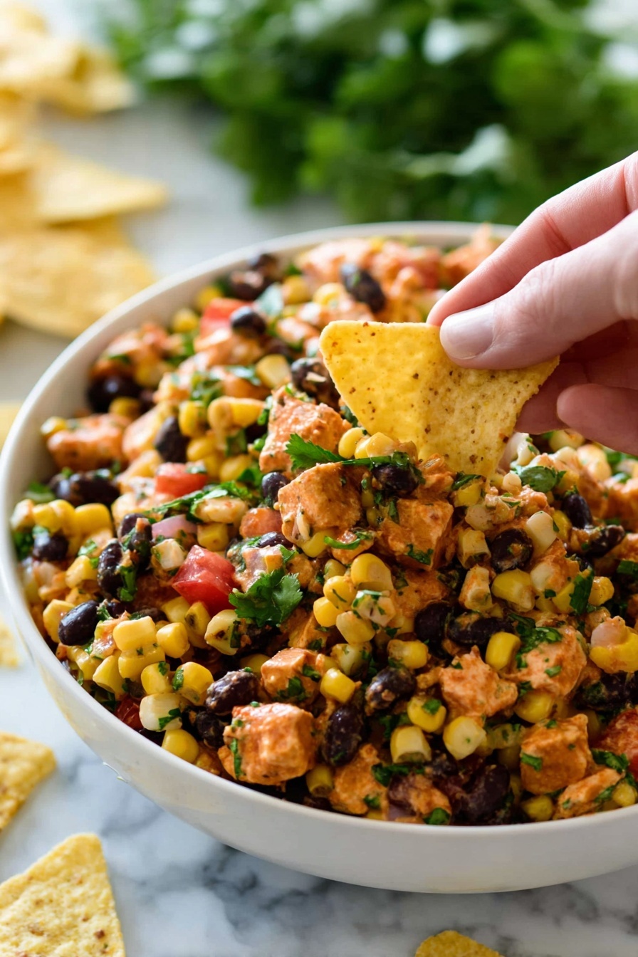 A white bowl is filled with a mixed salad containing small, yellow corn kernels, black beans, orange-colored diced pieces that look like chicken or tofu, and small bits of green herbs scattered on top. There are also small cubes of red tomato or bell pepper mixed in. A woman's hand is holding a pale yellow triangular tortilla chip, scooping some of the salad from the bowl. The background is a white marbled surface, and some green leafy vegetables can be seen blurred in the back along with a few tortilla chips scattered around the bowl. Photo taken with an iphone --ar 2:3 --v 7 - Southwest Chicken Salad, Mexican chicken salad, healthy chicken salad, easy dinner recipes, high-protein salads