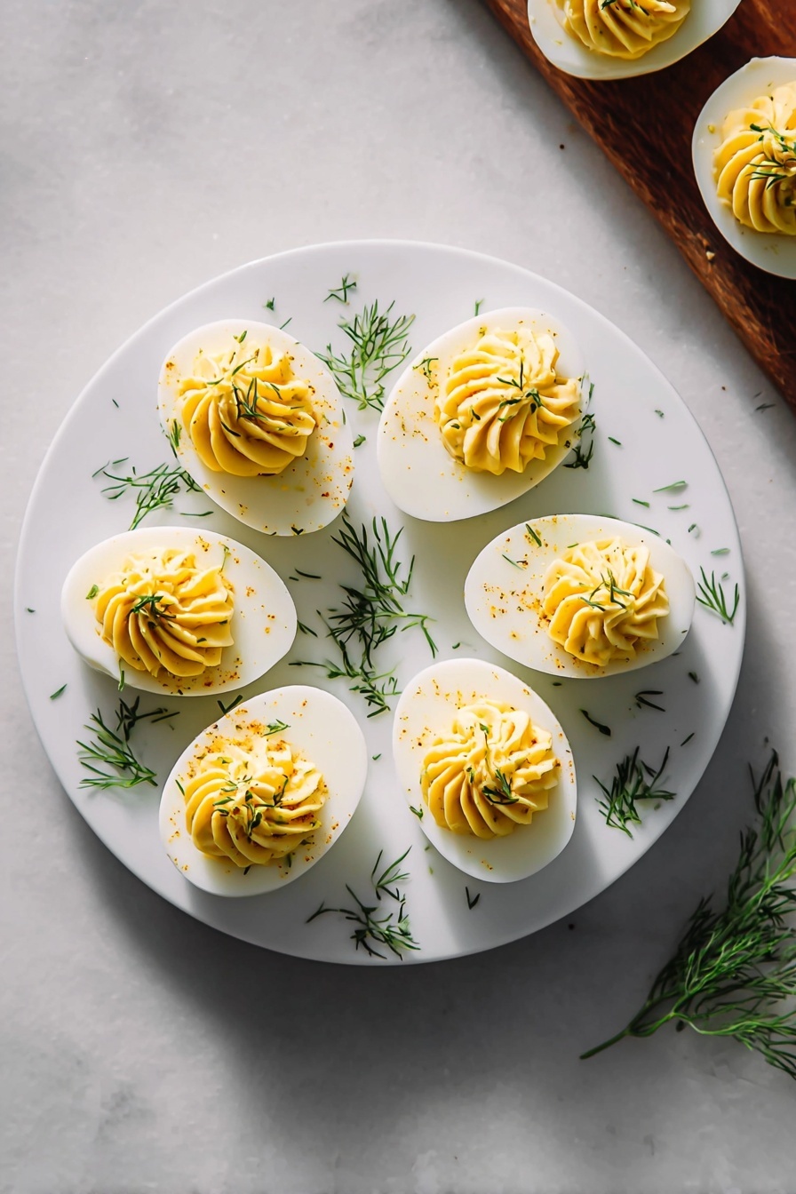 The image shows a white round plate on a white marbled surface. On the plate, there are six deviled egg halves arranged in a circle. Each deviled egg has a smooth white egg white base and a creamy, swirled yellow yolk filling on top, garnished with small green dill pieces sprinkled over and around the eggs. To the right side of the plate, there are three more deviled eggs partially visible on the same white marbled surface. Bright, natural light highlights the smooth textures and fresh garnishes, giving the dish a clean and appetizing look. Photo taken with an iphone --ar 2:3 --v 7 - Perfect Deviled Eggs, deviled eggs recipe, easy deviled eggs, party appetizer ideas, creamy deviled eggs