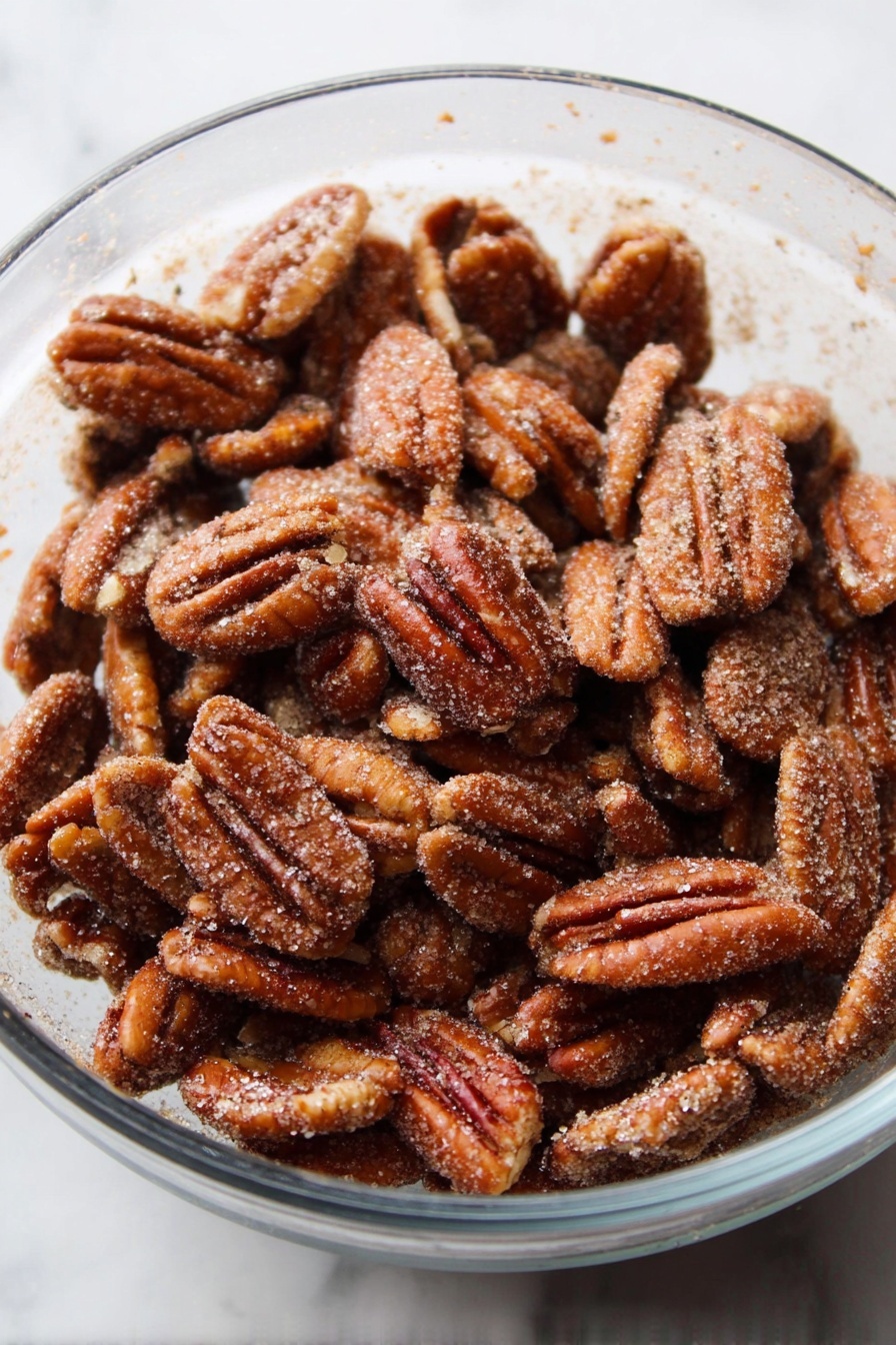 A clear glass bowl is full of many toasted pecan halves, each nut showing a rough, crinkled surface with a shiny brown color covered lightly with a layer of fine sugar crystals and cinnamon dust. The bowl sits on a white marbled surface. photo taken with an iphone --ar 2:3 --v 7 - Candied Cinnamon Pecans, cinnamon candied pecans, sweet spicy pecans, crunchy caramel pecans, easy candied nut recipes