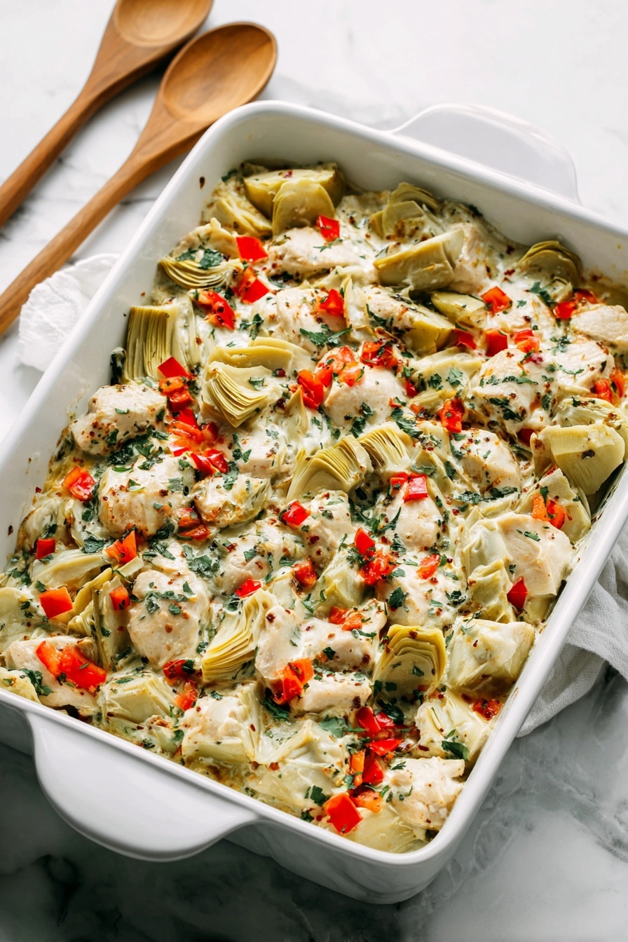 A white rectangular baking dish filled with a layered mix of creamy white sauce, pieces of light beige cooked chicken, and quartered pale green artichoke hearts. The dish is sprinkled with small, bright red bell pepper pieces and finely chopped dark green herbs, creating a colorful contrast. The textures range from creamy sauce to tender chunks of chicken and soft artichokes, all blended evenly across the dish. The dish sits on a white marbled surface with two wooden spoons with white handles placed behind it. Photo taken with an iphone --ar 2:3 --v 7 - Creamy Spinach Artichoke Chicken Bake, spinach artichoke chicken casserole, easy chicken bake, healthy chicken dinner, cheesy chicken bake