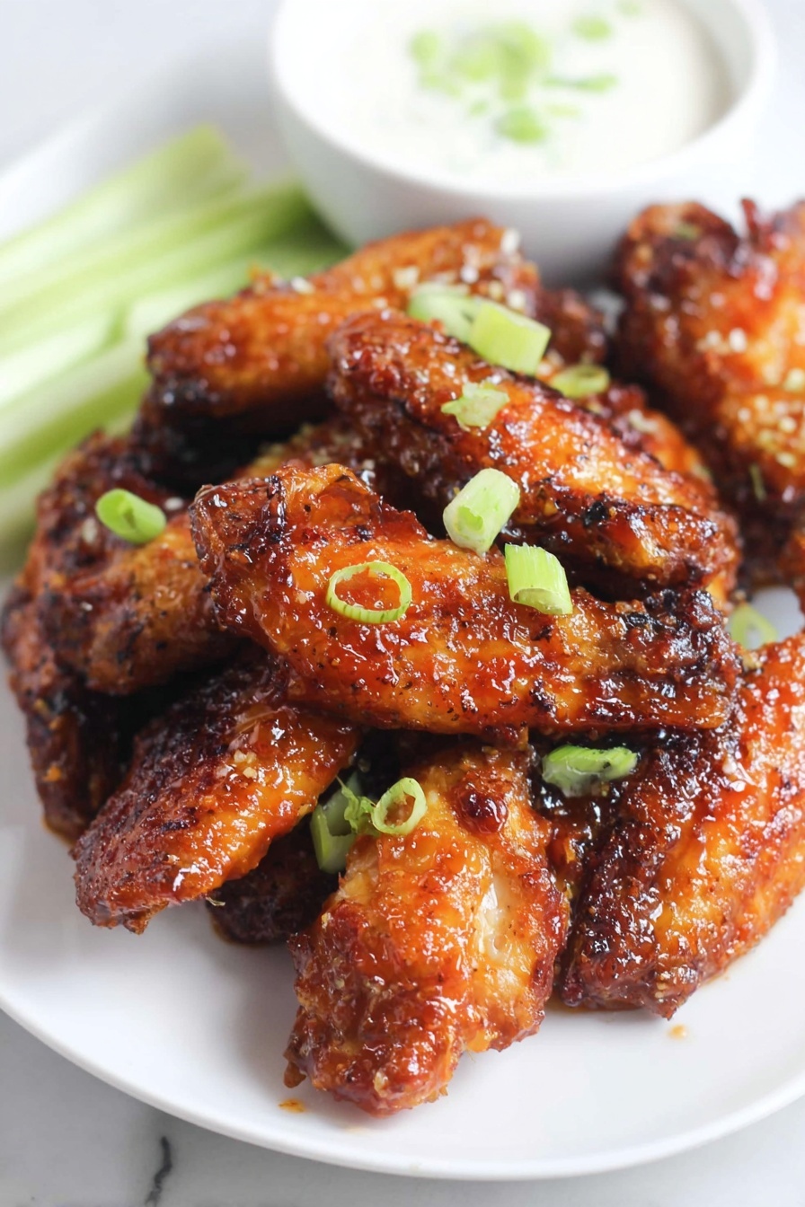 A white plate on a white marbled surface holds a pile of shiny, well-cooked chicken wings glazed with a sticky orange sauce, giving them a crisp and slightly charred texture. The wings are scattered with small bright green slices of green onion. Behind the wings on the plate, there is a small white bowl filled with a creamy, white dipping sauce. To the side of the bowl, light green celery sticks slightly peek into the frame. The scene is brightly lit, showing the rich colors and texture of the food clearly. photo taken with an iphone --ar 2:3 --v 7 - Honey Garlic Chicken Wings, Easy Honey Garlic Wings Recipe, Crispy Honey Garlic Chicken, Sweet and Savory Chicken Wings, Best Honey Garlic Wing Recipe