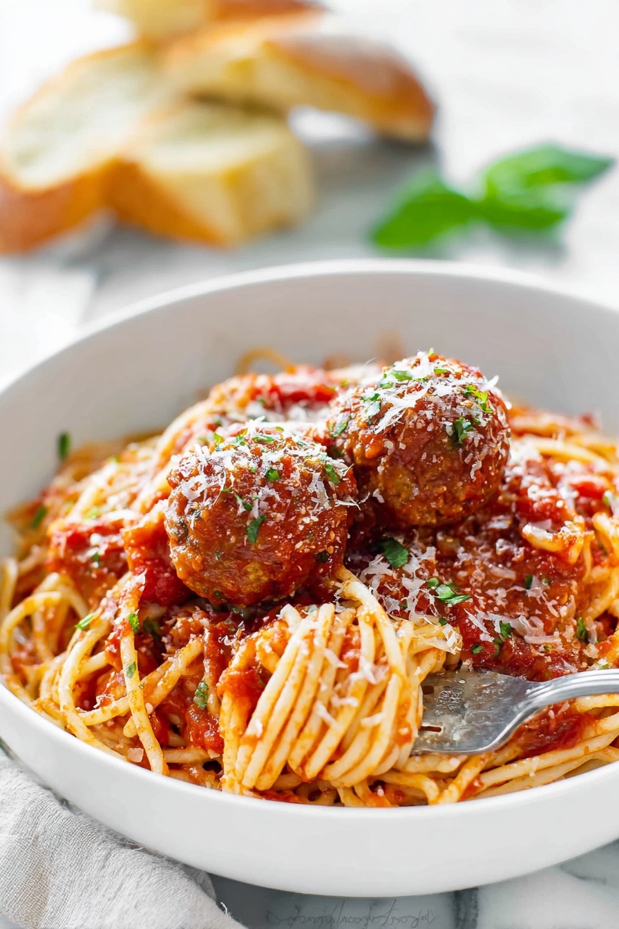 A large red pot holds a mix of spaghetti and meatballs in a rich tomato sauce. The spaghetti is long and golden, twisted around and soaked in the chunky red sauce. The meatballs are round and brown, scattered evenly through the noodles, some partially covered with sauce. A wooden spoon with a smooth light wood texture is stirring the pasta, with some sauce on it. The pot’s inside edge shows a coating of the thick tomato sauce. The background has a white marbled texture. photo taken with an iphone --ar 2:3 --v 7 - Homemade Spaghetti and Meatballs, Italian pasta with meatballs, easy spaghetti and meatballs, classic spaghetti and meatballs, hearty Italian dinner