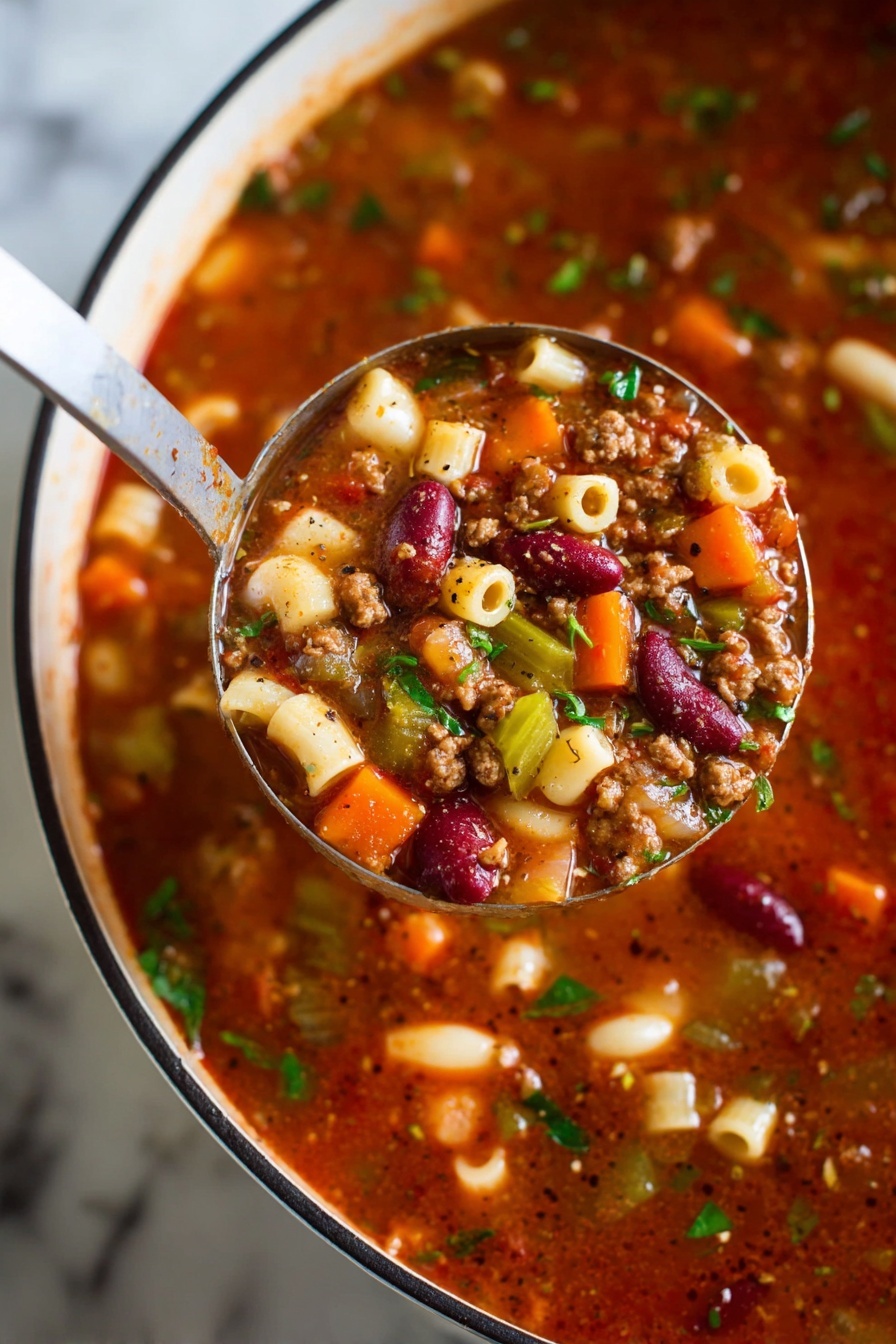 A close-up view of a ladle holding a rich, chunky soup above a white pot with a black rim, all resting on a white marbled surface. The soup has multiple layers visible: a thick, deep red broth base mixed with small bits of brown ground meat, bright orange carrot cubes, pale white and red kidney beans, green celery slices, and small round pasta pieces. Fresh green herbs are sprinkled throughout, adding a fresh touch. Black pepper flecks are visible on the surface of the soup and ladle, giving it a seasoned look. photo taken with an iphone --ar 2:3 --v 7 - Easy Pasta e Fagioli Soup, pasta e fagioli recipe, hearty Italian soup, quick pasta e fagioli, comforting bean and pasta soup