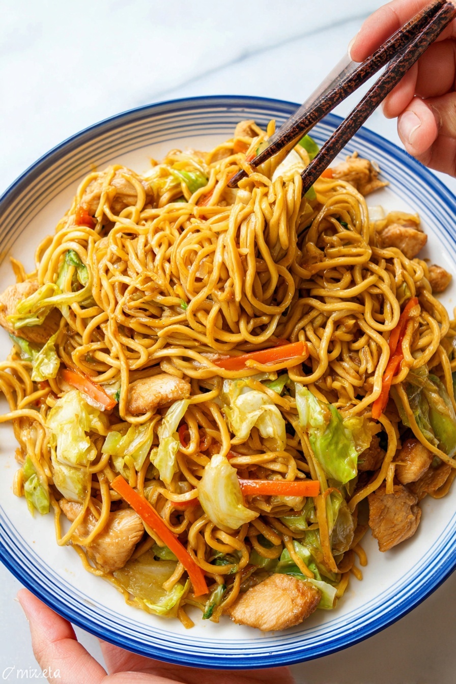 A white plate with a blue rim holds a serving of stir-fried noodles mixed with pieces of cooked light brown chicken, bright orange carrot sticks, and green cabbage leaves. The noodles are golden yellow and tangled together, with some lifted by dark brown chopsticks held by a woman's hand above the plate. The plate is on a white marbled surface, and the woman’s hand is seen at the bottom left corner holding the plate slightly. Photo taken with an iphone --ar 2:3 --v 7 - Easy Chicken Yakisoba Stir-Fry, Chicken Yakisoba recipe, Japanese stir-fry, quick chicken dinner, savory yakisoba dish
