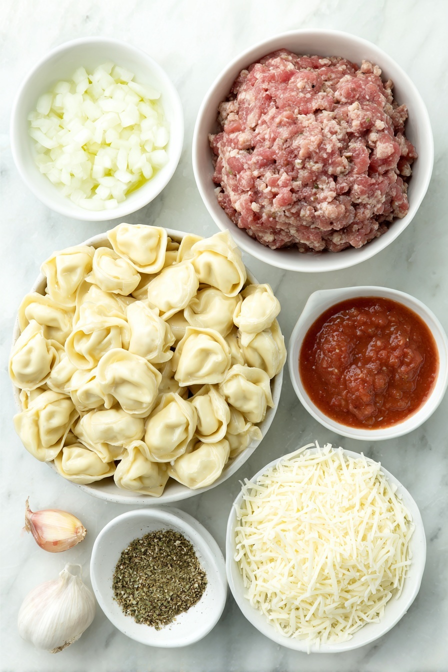 Flat lay of a mound of fresh cheese tortellini, a small white ceramic bowl of golden olive oil, a white ceramic bowl holding three whole uncracked brown garlic cloves, a small pile of finely diced white onion, a portion of raw lean ground beef shaped neatly, a white ceramic bowl filled with bright red crushed tomatoes, another white ceramic bowl with smooth red tomato sauce, a small heap of dried Italian seasoning herbs, coarse kosher salt crystals scattered lightly, a few twists of freshly ground black pepper, and a small white ceramic bowl heaped with freshly grated mozzarella cheese, all arranged in perfect symmetry on a clean white marble surface, soft natural light, photo taken with an iPhone, professional food photography style, fresh ingredients, white ceramic bowls, no bottles, no duplicates, no utensils, no packaging --ar 2:3 --v 7 --p m7354615311229779997 - Cheesy Baked Tortellini Casserole, baked tortellini recipes, cheesy pasta casserole, hearty tortellini dinner, easy baked pasta dishes