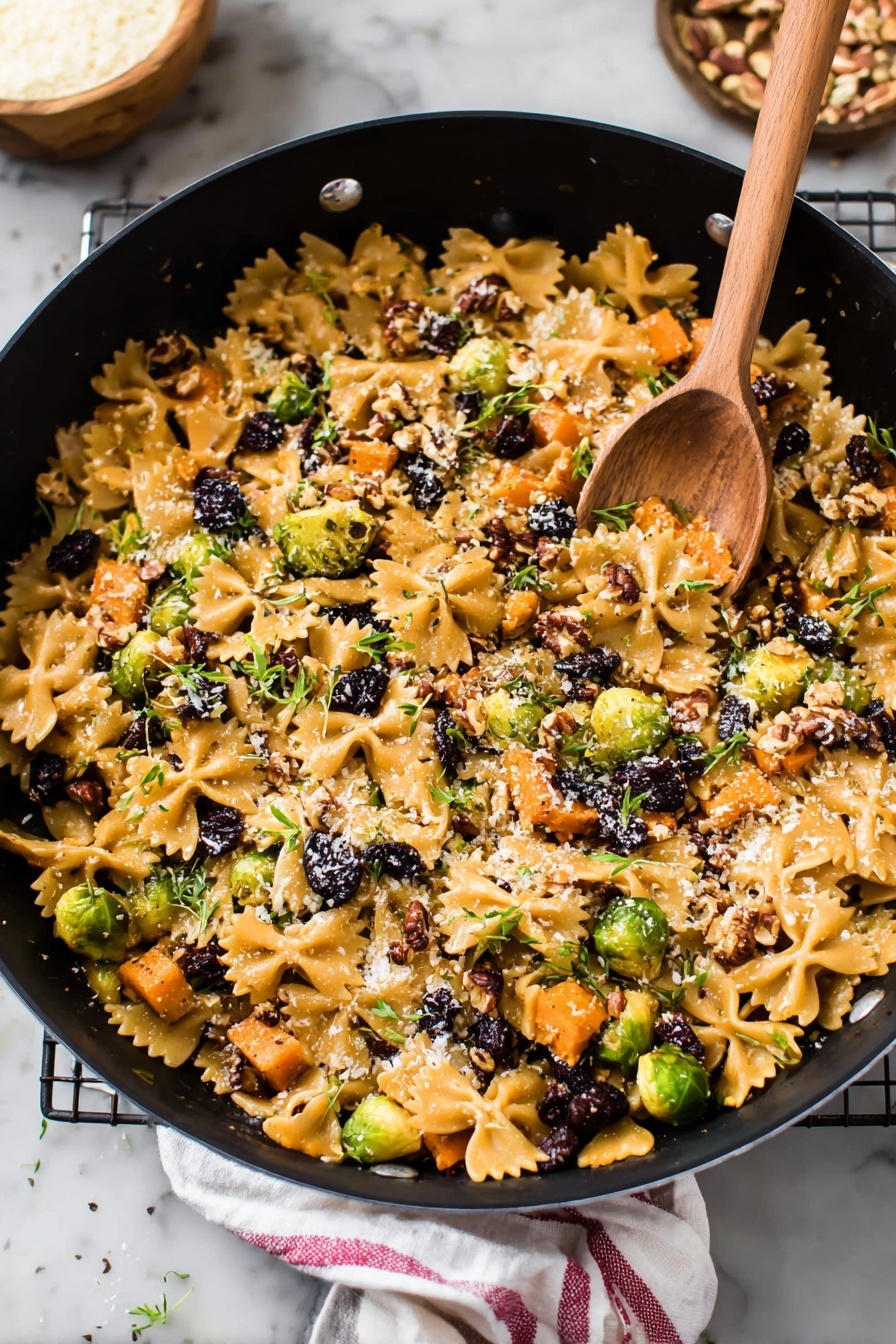 A large black pot filled with a colorful mix of farfalle pasta and small pieces of roasted orange sweet potatoes spread all over. Bright green Brussels sprouts cut in halves and small dark purple dried berries are scattered inside. There are bits of chopped pecans and a light sprinkle of grated cheese on top, with little green herb leaves spread around. In the pot, a wooden spoon rests on the food, and the scene is set on a white marbled surface, with some pecans and a small bowl of grated cheese nearby. A white cloth with a red stripe is partially visible next to the pot. Photo taken with an iphone --ar 2:3 --v 7 - Brussels Sprouts Pasta with Brown Butter, Brussels Sprouts Pasta, brown butter pasta recipes, fall vegetable pasta, easy weeknight pasta