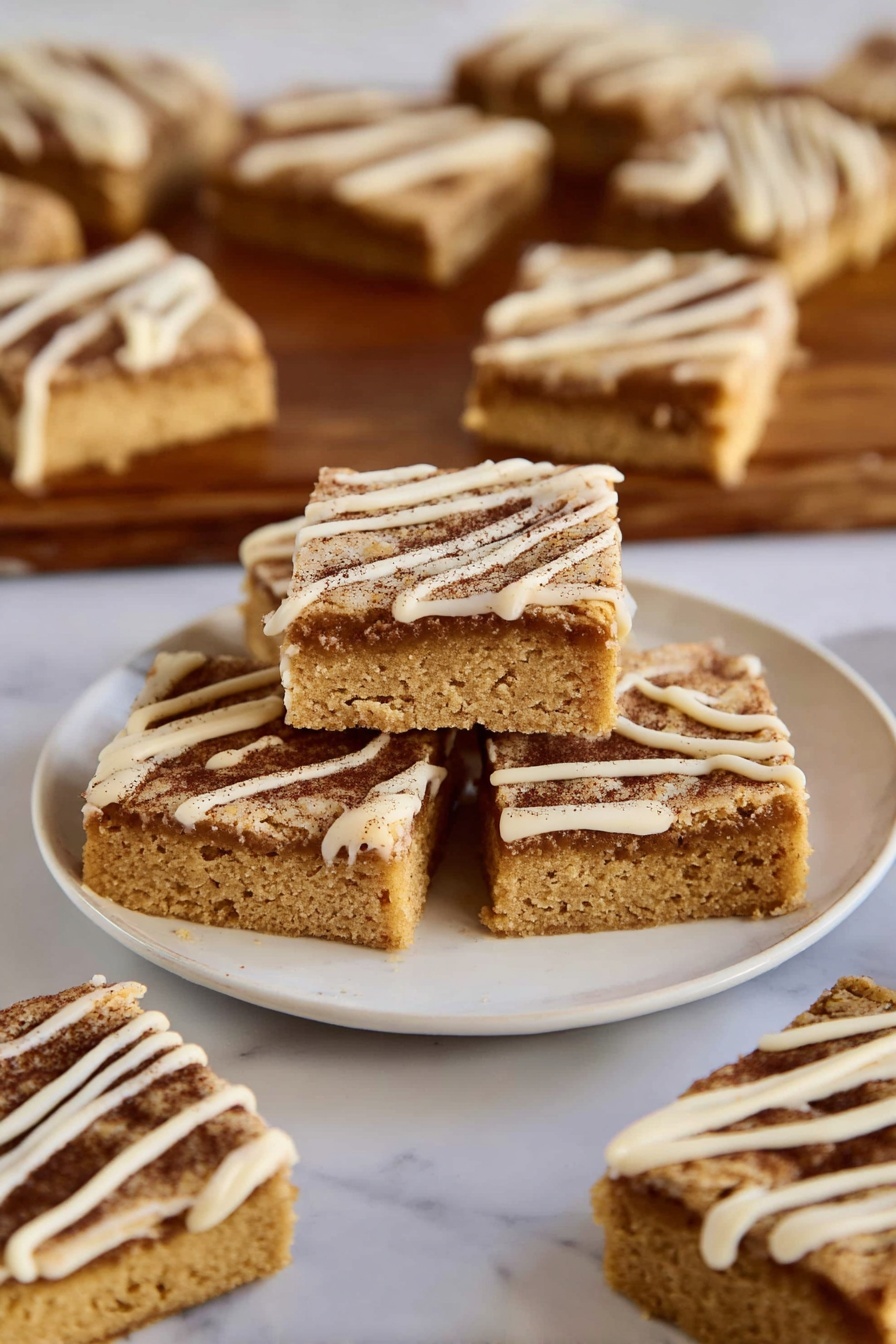 The image shows several square-shaped blondies with two visible layers: a thick golden-brown base with a soft texture and a darker cinnamon-brown sugar layer on top, sprinkled with a thin drizzle of creamy white icing forming diagonal lines. Three blondies are stacked in the center of a white plate, with more pieces spread around on the same plate and on a wooden board in the background, all placed on a white marbled surface. photo taken with an iphone --ar 2:3 --v 7 - Cinnamon Sugar Blondies, cinnamon blondies, easy blondie recipe, cinnamon dessert, sweet blondie bars