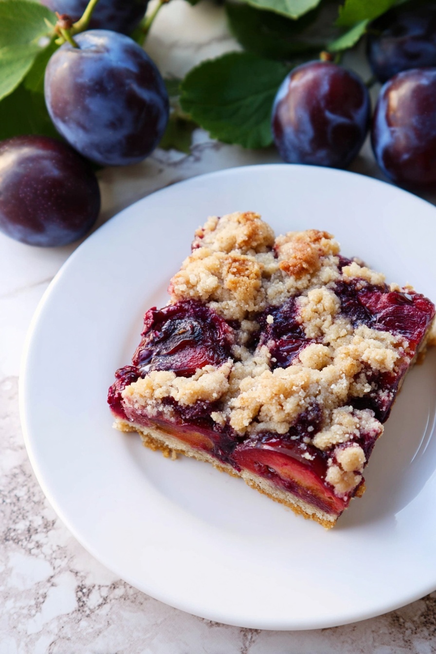 A square slice of a fruit crumble bar sits on a white plate. The bottom layer is a light golden crust, topped with a thick layer of dark red and purple cooked plums showing a soft texture. The top layer is a crumbly streusel with uneven pieces of pale beige and light brown. The plate is placed on a white marbled surface, next to fresh whole dark purple plums with green leaves. Photo taken with an iphone --ar 2:3 --v 7 - German Plum Cake with Yeast Dough, traditional Zwetschgenkuchen, German fruit cake, yeast dough plum tart, German dessert with plums