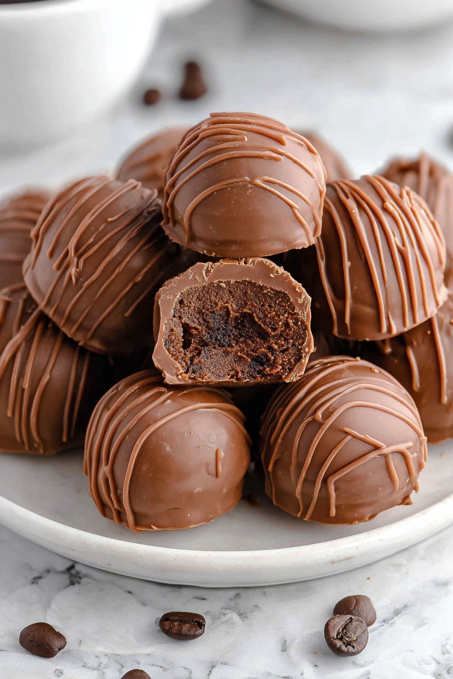 A white plate filled with round milk chocolate truffles, each truffle covered with thin milk chocolate drizzle lines on top. One truffle is broken in half and placed on top of the others, showing a thick, darker chocolate center with a smooth and slightly crumbly texture inside. The plate is on a white marbled surface with a few dark brown coffee beans scattered around. Photo taken with an iphone --ar 2:3 --v 7 - Delicious Coffee Chocolate Truffles, coffee chocolate truffles, easy chocolate truffles, coffee-flavored desserts, gourmet chocolate treats