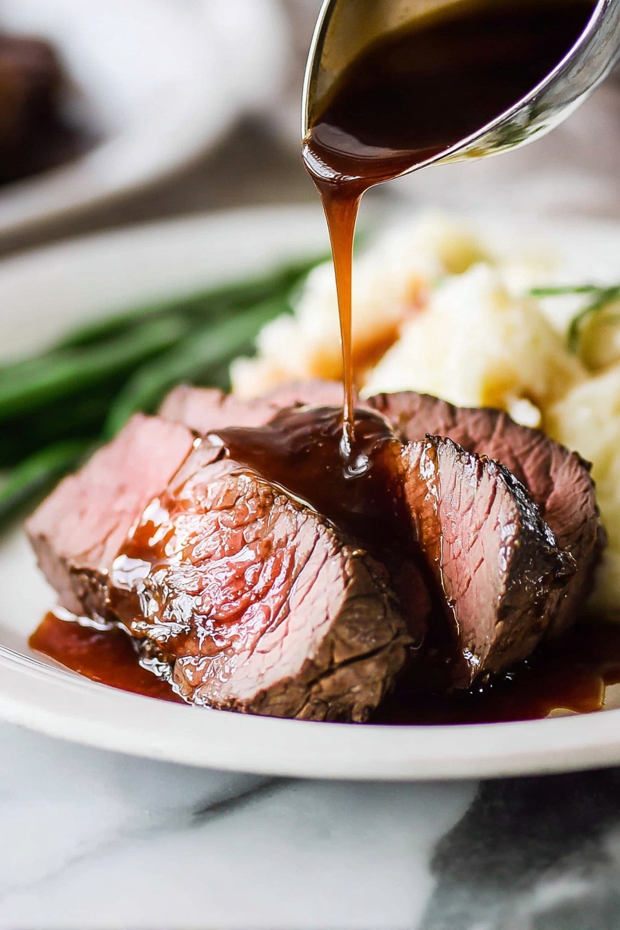 The image shows two thick slices of medium-rare roast beef placed on a white plate with a white marbled surface in the background. The roast beef has a brown crust on the outside and a pink center. A dark brown gravy sauce is being poured over the top slice from a ladle, creating a shiny texture with some sauce pooling on the plate. Behind the beef, there is a serving of creamy mashed potatoes and a few green beans slightly blurred in the background. The focus is on the meat and sauce with a close-up view emphasizing the moist texture of the beef and the rich shine of the gravy. Photo taken with an iphone --ar 2:3 --v 7 - Beef Tenderloin with Red Wine Sauce, beef tenderloin recipe, red wine steak sauce, elegant beef dinner, easy gourmet beef dish