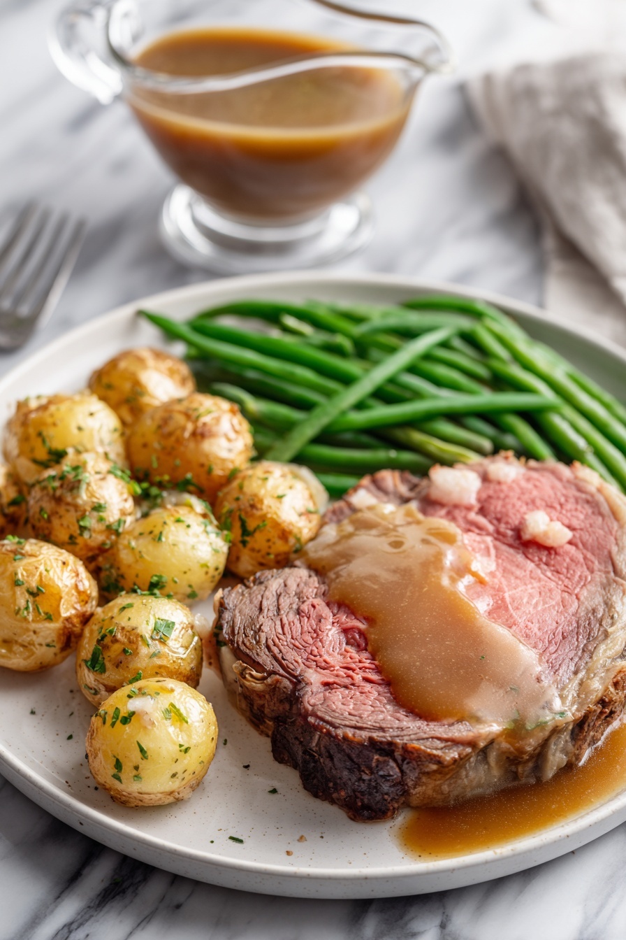 A white plate on a white marbled surface holds a meal with three main parts: a thick, medium-rare roast beef slice with a pink center and browned edges, topped with brown gravy that also pools around it; next to it, a pile of roasted small potatoes with golden brown skins sprinkled with green herbs; and a bunch of bright green cooked green beans laid neatly beside the potatoes. In the background, there is a clear glass gravy boat filled with brown gravy on the white marbled surface. photo taken with an iphone --ar 2:3 --v 7 - Garlic Herb Butter Prime Rib, prime rib recipe, roast beef with garlic herb butter, tender prime rib, holiday beef main dish
