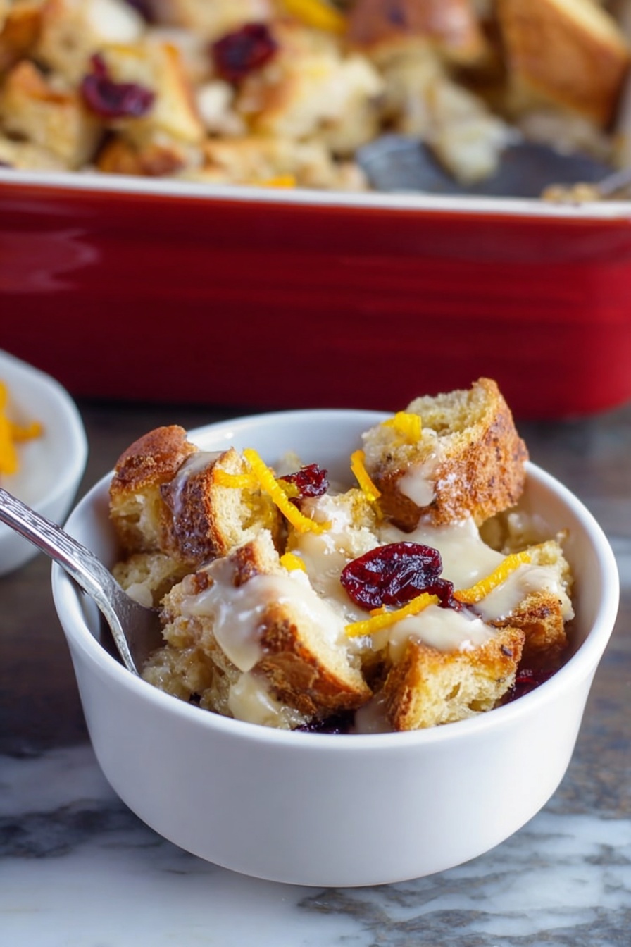 A small white bowl filled with several uneven layers of toasted bread pieces that are golden brown and crispy, mixed with a creamy, light-colored sauce spread unevenly throughout, topped with a few dried red cranberries and thin strips of bright orange zest, placed on a white marbled surface with a silver spoon inside the bowl, a larger baking dish filled with similar bread pudding in the background, photo taken with an iphone --ar 2:3 --v 7 - Cranberry Bread Pudding with Toffee Bits, Cranberry Bread Pudding, Holiday Bread Pudding, Toffee Bits Dessert, Easy Cranberry Bread Pudding