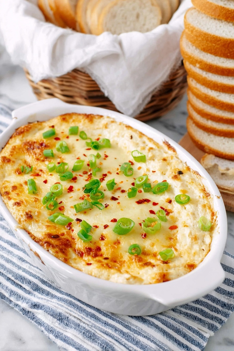 A white oval dish holds a baked dip with a top layer of melted golden cheese, sprinkled with small green spring onion rings and red chili flakes evenly spread. The dish rests on a folded striped blue and white cloth which is on a white marbled surface. To the right of the dish, a stack of sliced round white bread is arranged vertically. In the background, there is a basket with light brown bread lined with a white cloth. Photo taken with an iphone --ar 2:3 --v 7 - Cheesy Roasted Cauliflower Dip, healthy cauliflower dip, cheesy appetizer, easy vegetable dip, crowd-pleasing dip