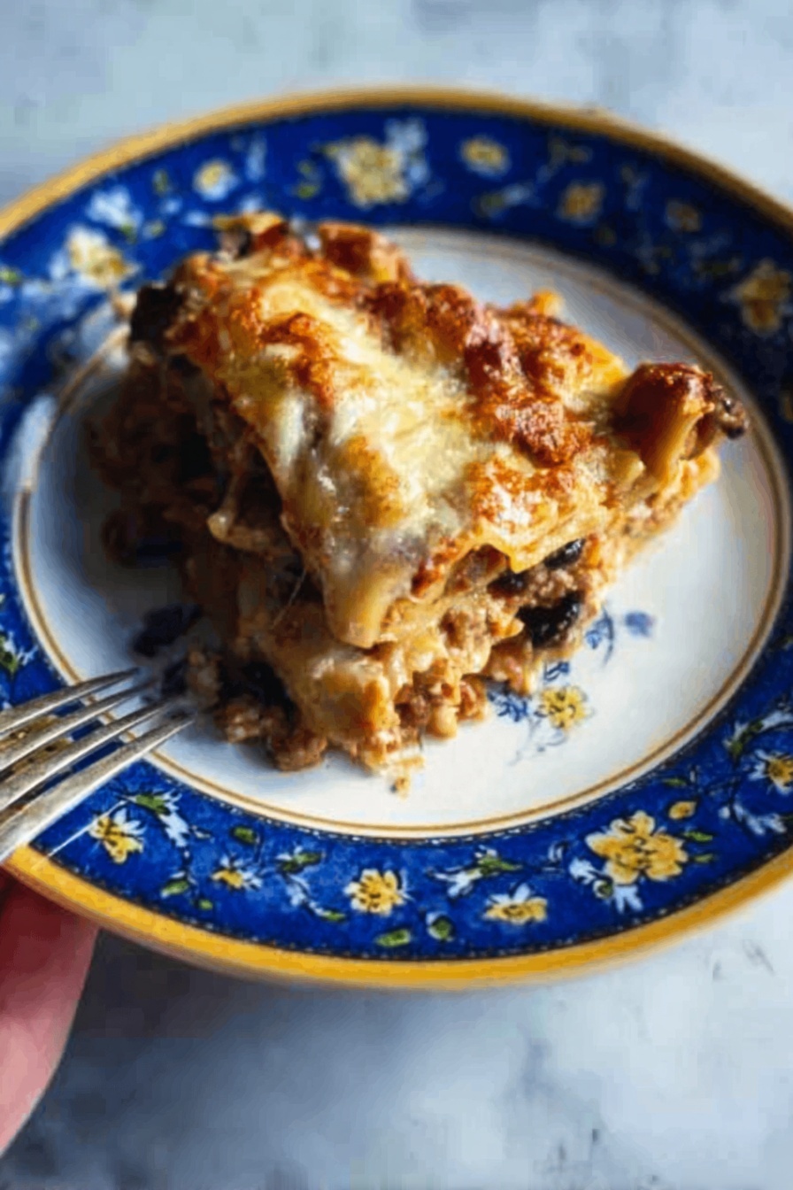 The image shows a close-up of a white plate with a blue and yellow floral pattern around the edge, holding a layered slice of lasagna. The lasagna slice has visible layers of browned melted cheese on top, a rich tomato sauce with ground meat and mushrooms below, followed by pale pasta sheets in between. A woman's hand with a fork is positioned to the side, ready to take a bite. The plate is on a white marbled surface. photo taken with an iphone --ar 2:3 --v 7 - Vegetarian Hatch Chile Enchiladas, Hatch Chile Enchiladas, Vegetarian Enchiladas with Hatch Chiles, Easy Hatch Chile Enchiladas, Roasted Hatch Chile Enchiladas