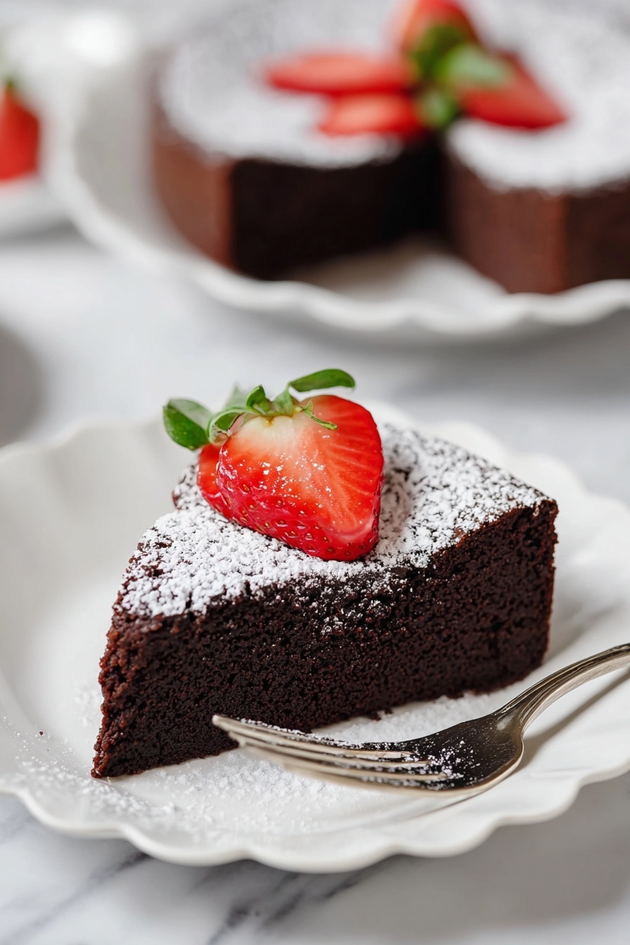 A single slice of dark brown chocolate cake with a soft, moist texture sits on a white scalloped plate. The top is dusted with a layer of white powdered sugar, and on top is a bright red sliced strawberry, fanned out with the green leafy top still attached. A silver fork rests on the right side of the plate. In the background, another slice of the same cake on a white scalloped plate is slightly blurred, all set on a white marbled surface. photo taken with an iphone --ar 2:3 --v 7 - Decadent Flourless Chocolate Cake, rich chocolate cake, fudgy chocolate dessert, easy chocolate cake recipe, elegant chocolate cake