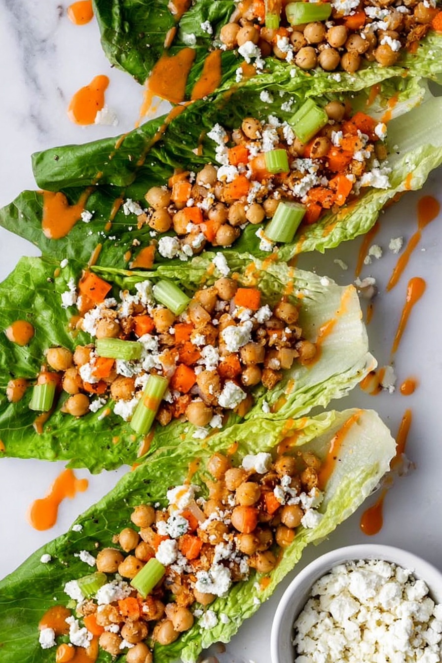 Two pieces of green romaine lettuce are placed side by side on a white marbled surface. Each lettuce leaf is filled with a mixture of round, light brown chickpeas, small diced orange carrots, tiny bits of white cheese, and small green celery pieces. The chickpeas form the main layer on each leaf, with the carrots and cheese sprinkled throughout, and a few celery leaves sticking out. A light drizzle of orange sauce is spread over the top of the filling. photo taken with an iphone --ar 2:3 --v 7 - Buffalo Chickpea Salad, spicy vegan salad, quick vegetarian lunch, healthy chickpea salad, buffalo wing inspired salad