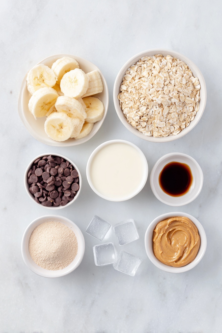 Flat lay of a peeled frozen banana sliced into chunks, a small white ceramic bowl filled with whole rolled oats, a dollop of natural peanut butter neatly placed on a white ceramic dish, a small white bowl containing unsweetened almond milk, a few clear ice cubes arranged near the bowls, a small white bowl holding vanilla protein powder, a neatly rounded heap of maca powder on a white plate, a splash of cold brew coffee shown as a small amount of dark liquid in a white bowl, and a small white bowl with glossy chocolate chips, all placed symmetrically on a clean white marble surface, soft natural light, photo taken with an iPhone, professional food photography style, fresh ingredients, white ceramic bowls, no bottles, no duplicates, no utensils, no packaging --ar 2:3 --v 7 --p m7354615311229779997 - Peanut Butter Banana Smoothie, healthy smoothie recipes, quick breakfast drinks, energy-boosting smoothies, creamy banana peanut butter blend