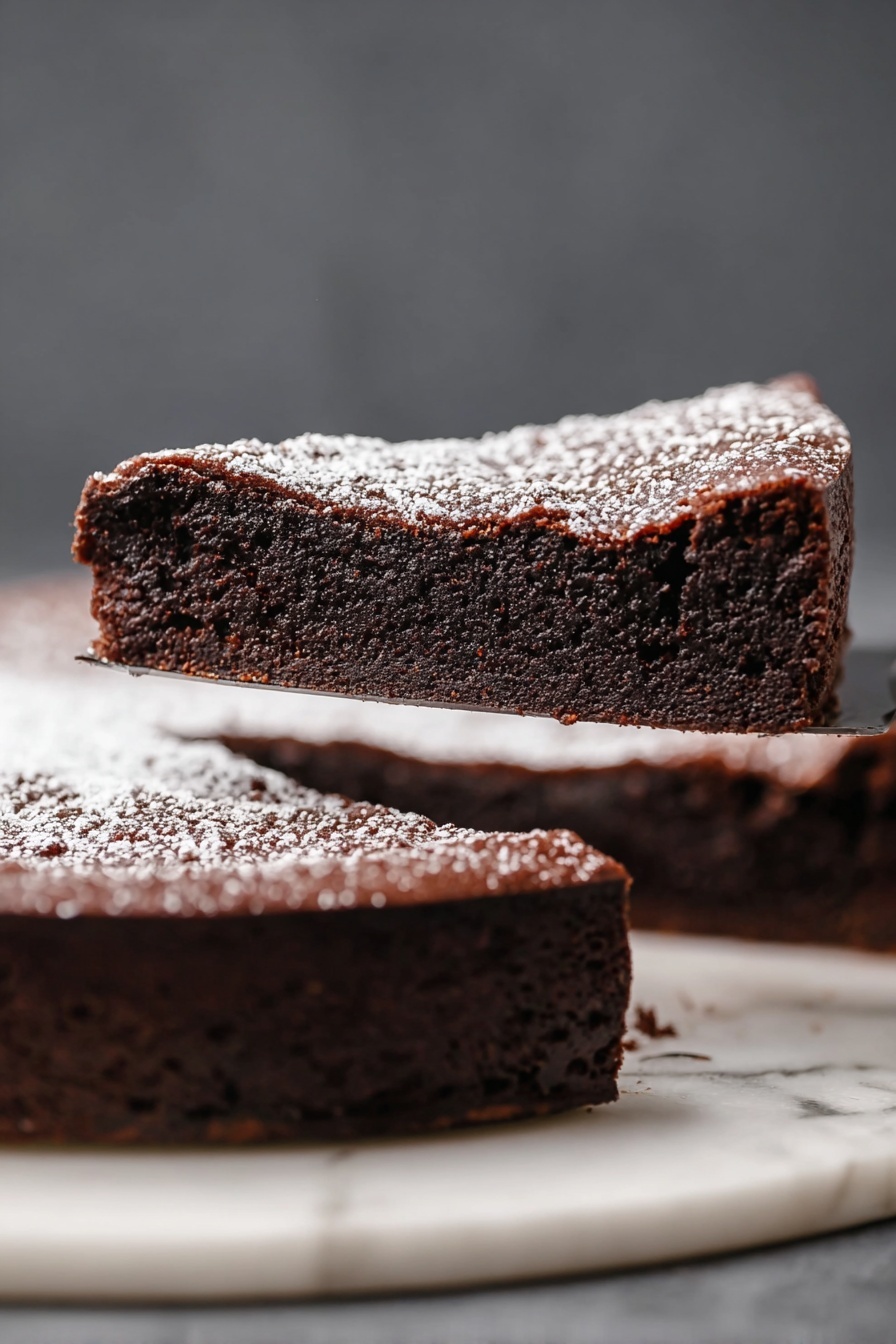 The image shows a thick slice of dark brown chocolate cake with a slightly cracked top layer sprinkled with light white powdered sugar. The slice is lifted above a whole round cake of the same color and texture, resting on a white marbled surface. The cake looks moist and dense, with even texture throughout and clean edges. The background is a soft dark gray tone. Photo taken with an iphone --ar 2:3 --v 7 - Decadent Flourless Chocolate Cake, rich chocolate cake, fudgy chocolate dessert, easy chocolate cake recipe, elegant chocolate cake