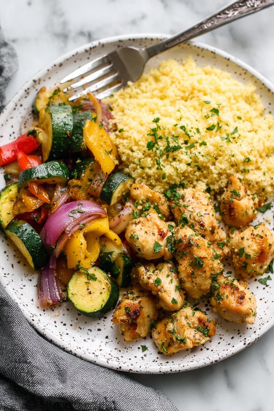 The dish on a white speckled round plate features three clear sections. On the right are small pieces of golden-brown cooked chicken sprinkled with chopped green herbs. In the middle section, there is light yellow couscous with a fluffy texture. On the left, there is a mix of sautéed vegetables including green zucchini slices, yellow squash slices, red bell pepper pieces, and purple onion chunks, all seasoned and slightly shiny. A silver fork rests on the top edge of the plate with part of its handle visible. The background shows a white marbled surface and a gray fabric partially in view. Photo taken with an iphone --ar 2:3 --v 7 - Garlic Butter Chicken Bites, chicken dinner ideas, quick chicken recipes, easy garlic chicken, gourmet chicken bites