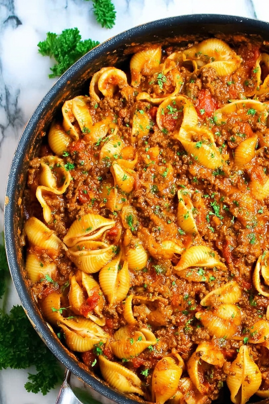 A close-up view of a large black pan filled with cooked yellow shell pasta mixed with a thick brown meat sauce, showing bits of red tomato and green herbs scattered evenly on top, the shells are soft and coated with the sauce, all placed on a white marbled surface with some green parsley leaves around the pan photo taken with an iphone --ar 2:3 --v 7 - Creamy Beef Pasta Shells, creamy beef pasta recipe, easy pasta dishes, comforting weeknight dinners, cheesy beef pasta