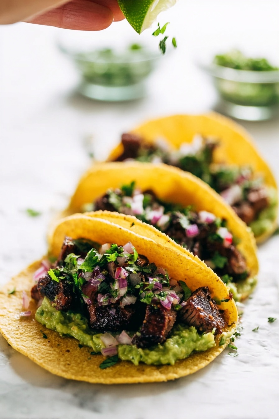 Three tacos are lined up on a white marbled surface, each taco made with a yellow corn tortilla that holds several layers. The bottom layer is chunky green guacamole, topped with small pieces of grilled dark brown meat with a slightly charred texture. Sprinkled over the meat are small bits of fresh green cilantro and finely chopped pinkish-red onions. Above the tacos, a woman's hand is squeezing a fresh lime wedge, adding a bright green color and a juicy texture to the scene. The background is softly blurred with clear glass bowls holding more chopped herbs and onions. Photo taken with an iphone --ar 2:3 --v 7 - Marinated Mojo Steak Tacos, steak tacos with citrus marinade, flavorful taco recipes, easy steak tacos, savory taco fillings