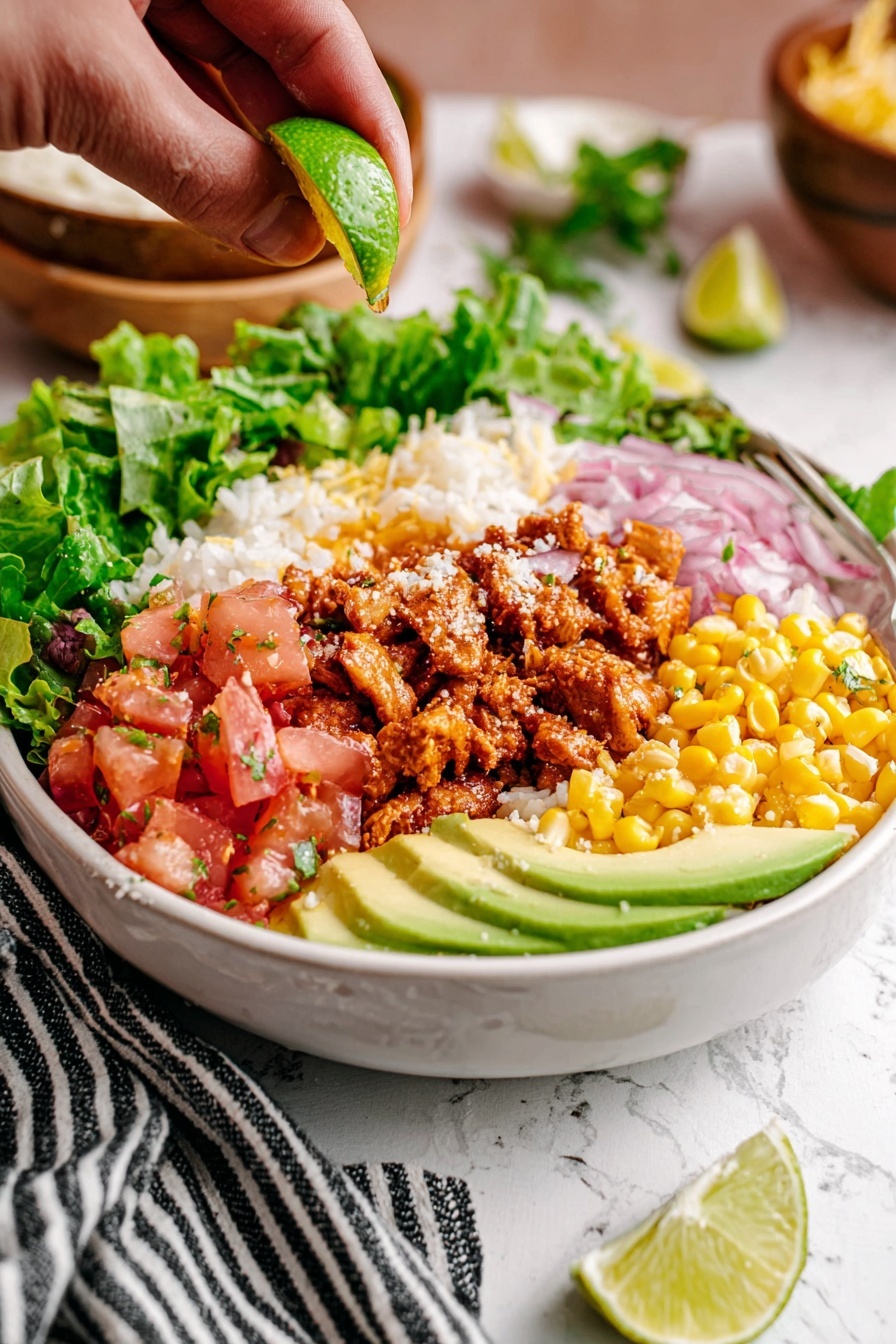 A close-up of a white bowl filled with a colorful layered salad sitting on a white marbled surface with a black and white striped cloth nearby; the bowl holds a base layer of white rice, topped on one side with bright green leafy lettuce spilling over the edge, next to diced red and orange tomatoes mixed with small yellow corn kernels, sprinkled lightly with crumbled white cheese; thin slices of avocado with a smooth light green color are arranged in a neat fan shape on one side, while opposite are reddish-brown chunks of cooked seasoned meat; thin purple onion slices are scattered lightly between layers, and a woman's hand is squeezing fresh lime juice over the dish from above, a lime wedge resting on the rim of the bowl; the background shows soft focus bowls and a light tan brick wall. photo taken with an iphone --ar 2:3 --v 7 - Street Corn Chicken Rice Bowl, street corn chicken bowl, Mexican street corn rice bowl, flavorful chicken rice bowl, easy weeknight dinner recipes