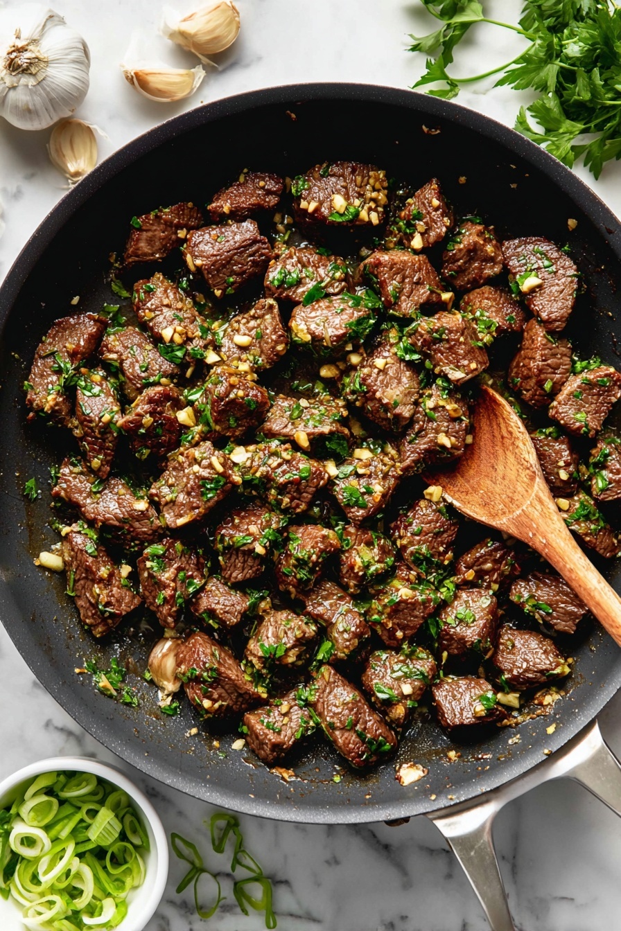 The image shows a black frying pan filled with many evenly sized pieces of cooked beef, browned on the outside. Each piece is covered with small bits of garlic and sprinkled with fresh green herbs, mostly chopped parsley. In the pan is a wooden spoon stirring the beef. Around the pan on a white marbled surface are garlic cloves, some green herbs, and a small white bowl with sliced green onions. The colors in the dish include dark brown from the beef, light golden from the garlic, and bright green from the herbs. Photo taken with an iphone --ar 2:3 --v 7 - Garlic Butter Steak Bites, steak bites recipe, quick steak dinner, easy steak appetizer, tender steak tips